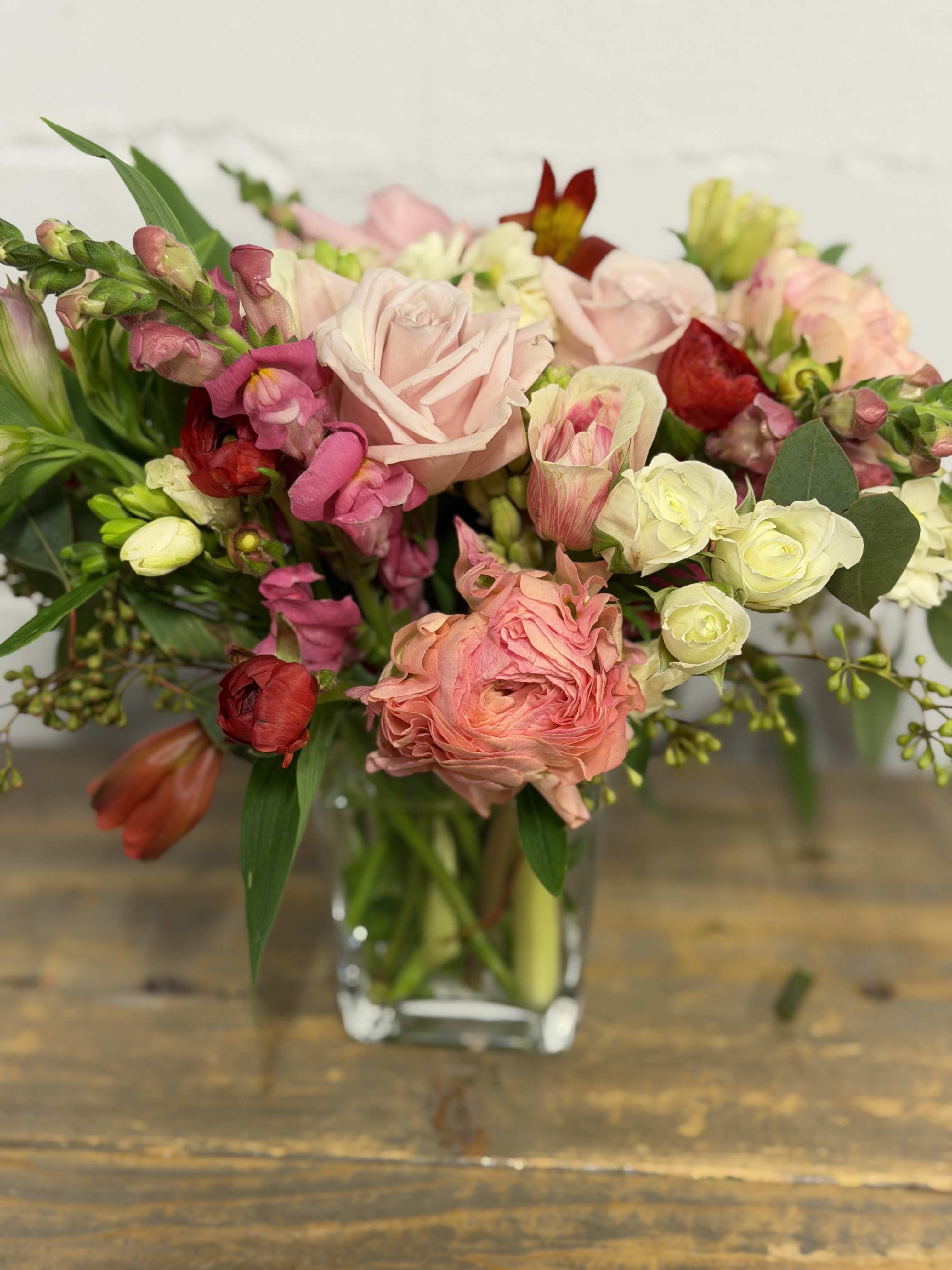 Mixed bouquet of pink, peach, and white flowers in a clear glass vase