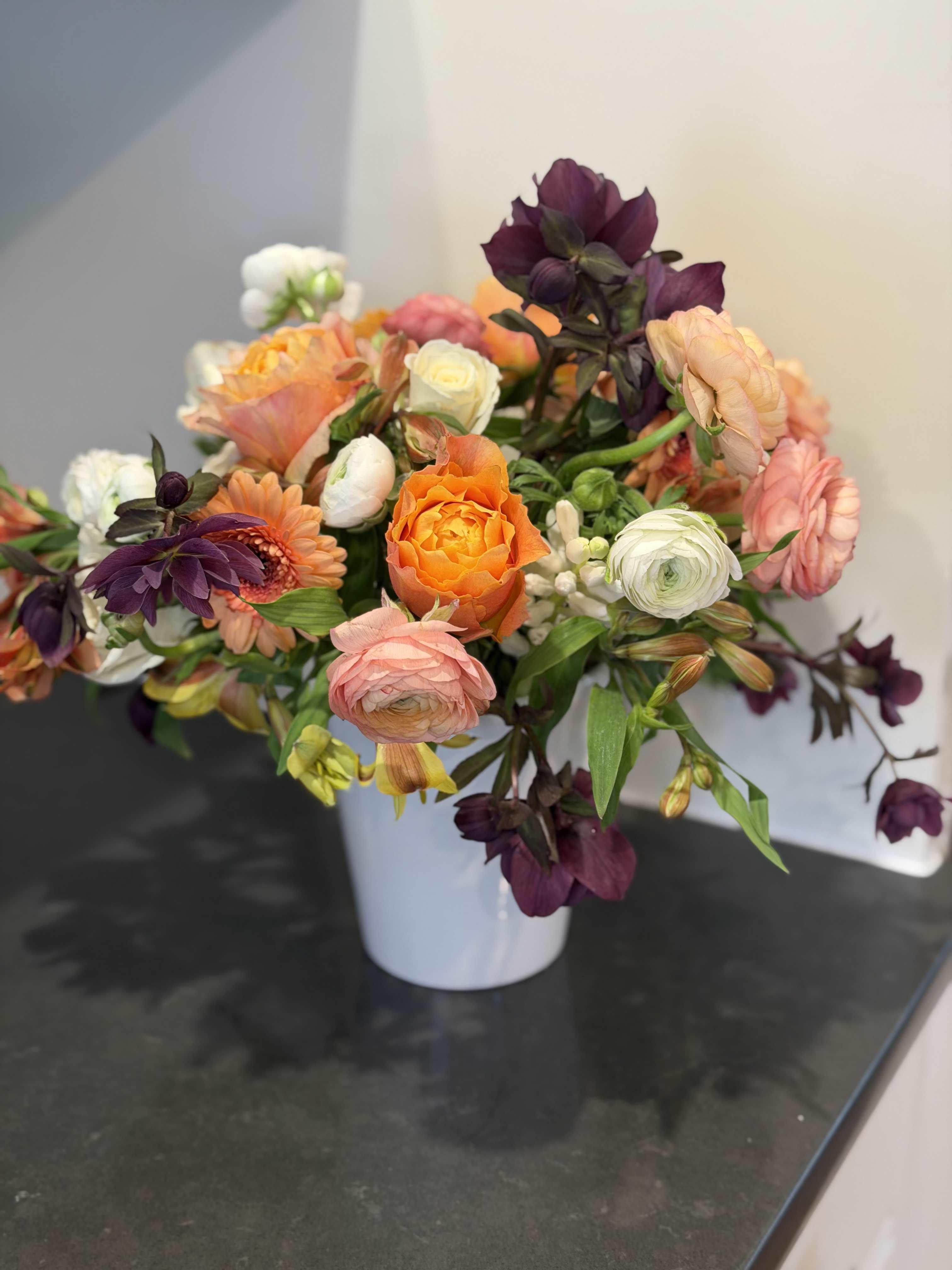 Mixed bouquet of orange, pink, white, and purple flowers in a white vase