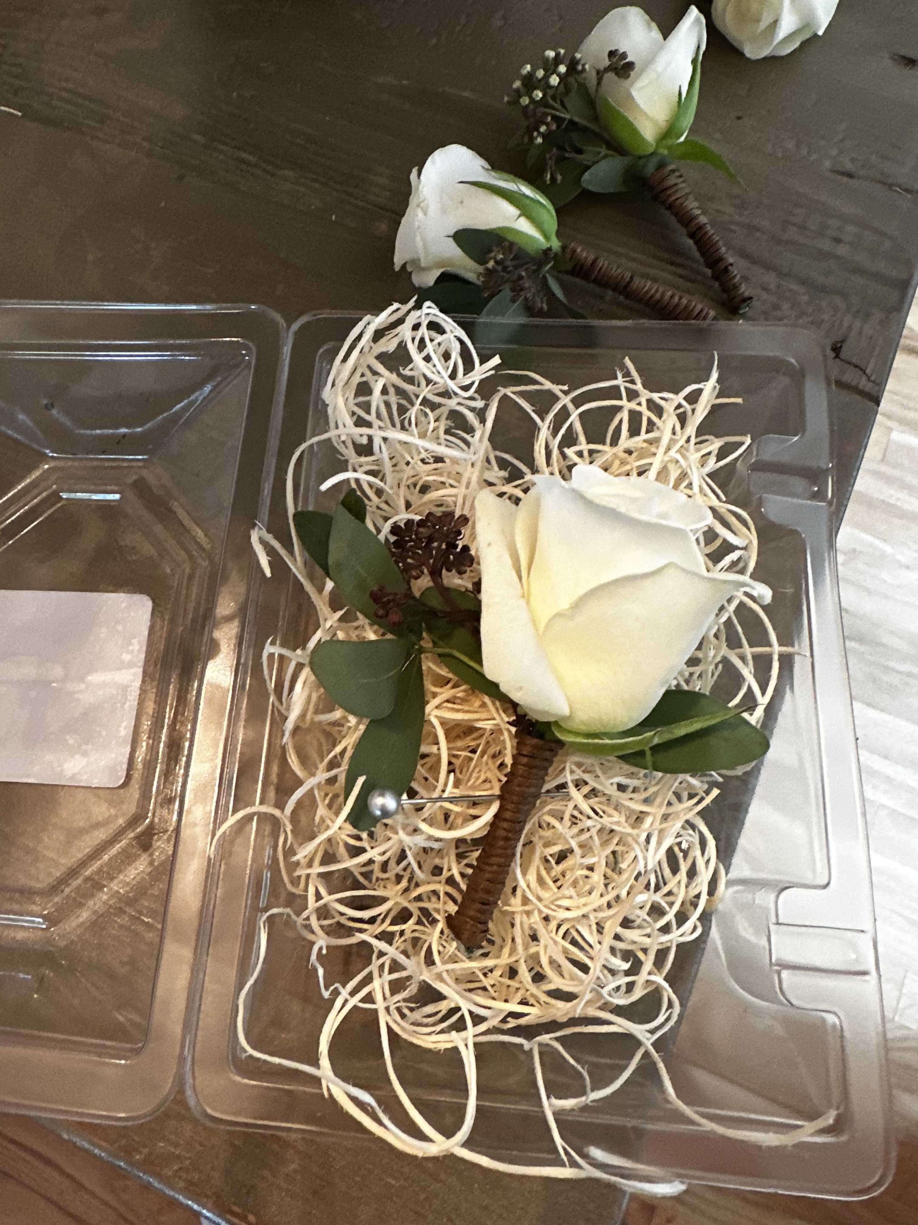 White rose boutonnieres in clear plastic packaging with straw filler.
