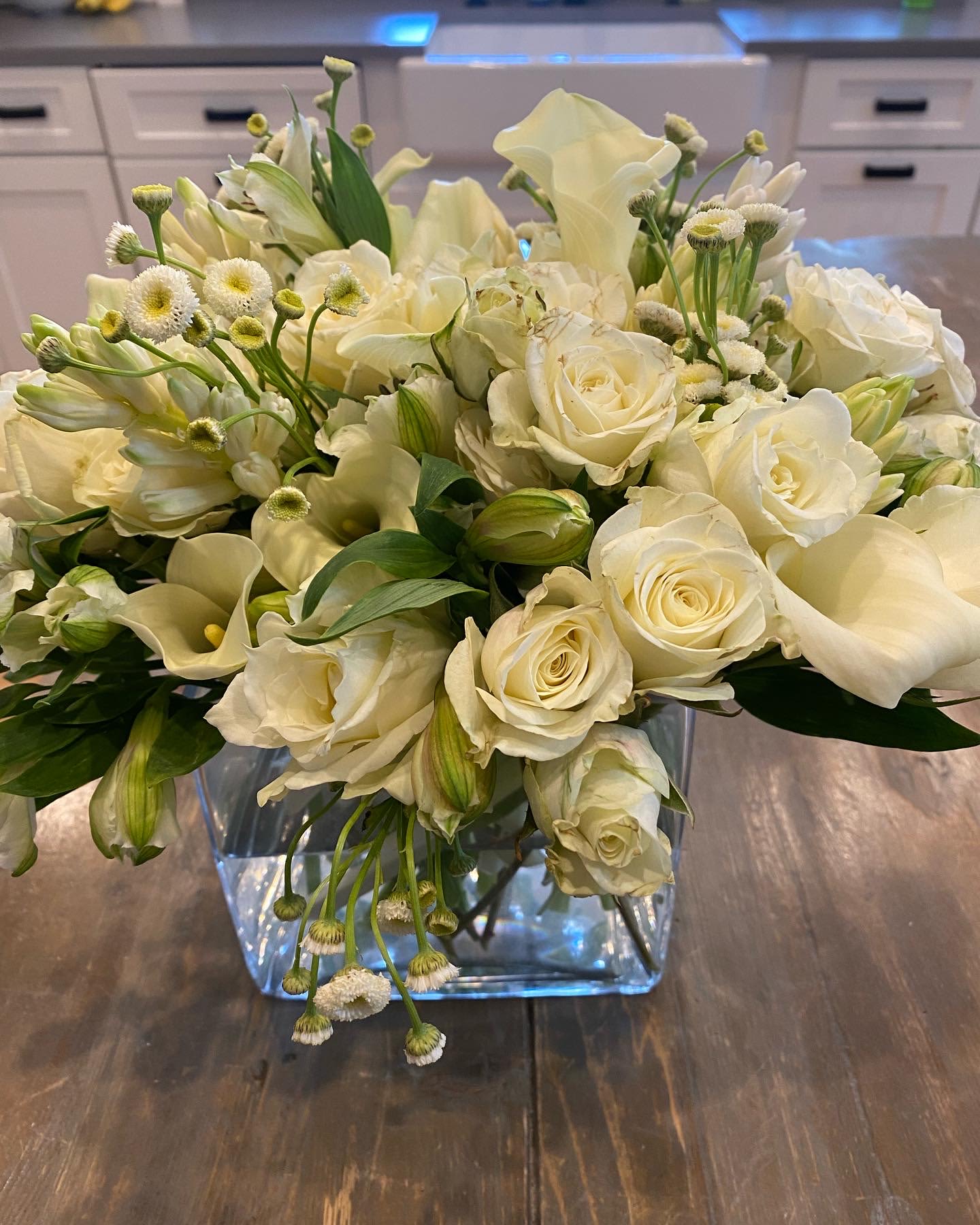 White roses and calla lilies arranged in a clear square vase