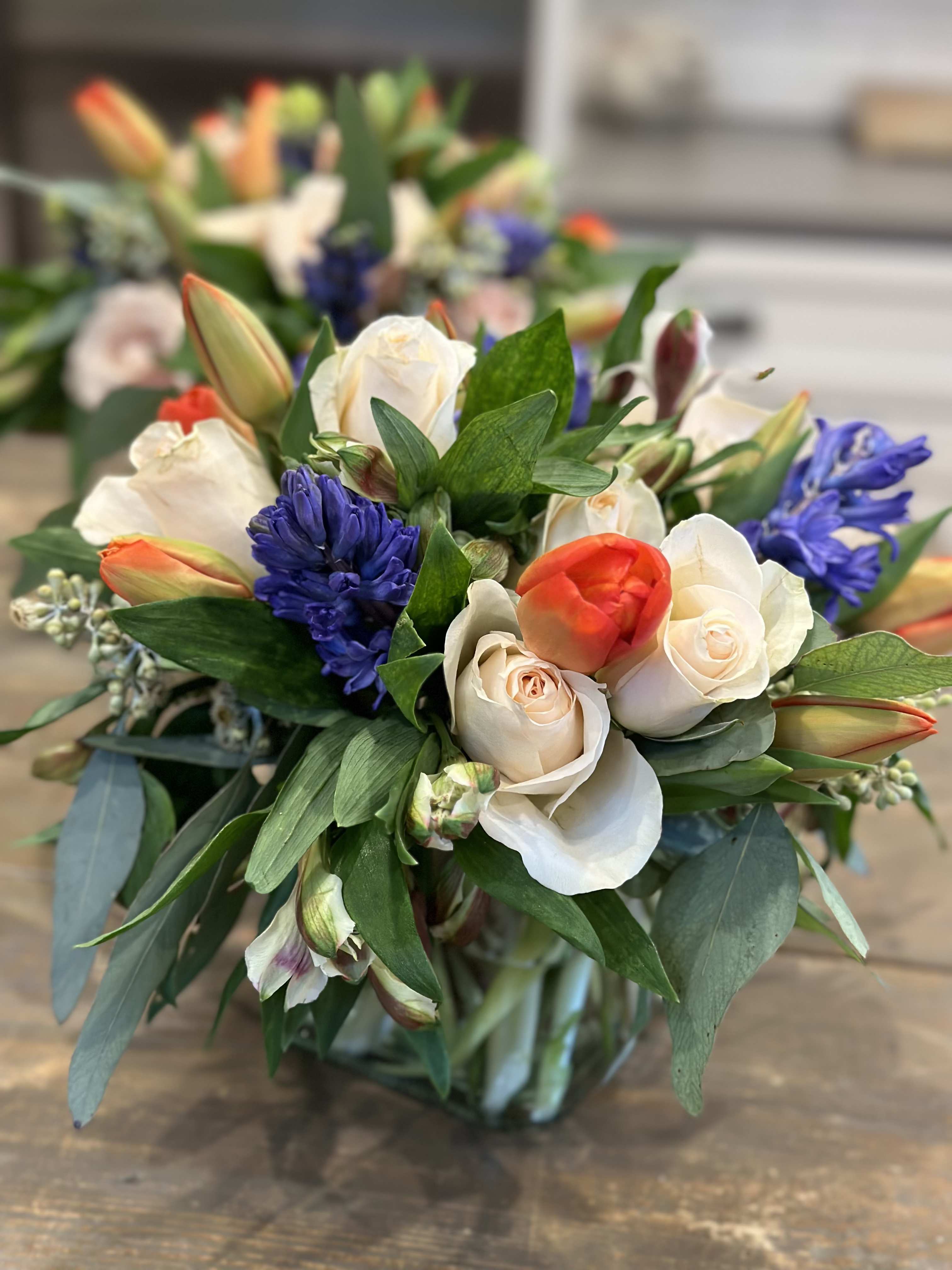 Bouquet of white roses, orange tulips, and blue hyacinths in a glass vase