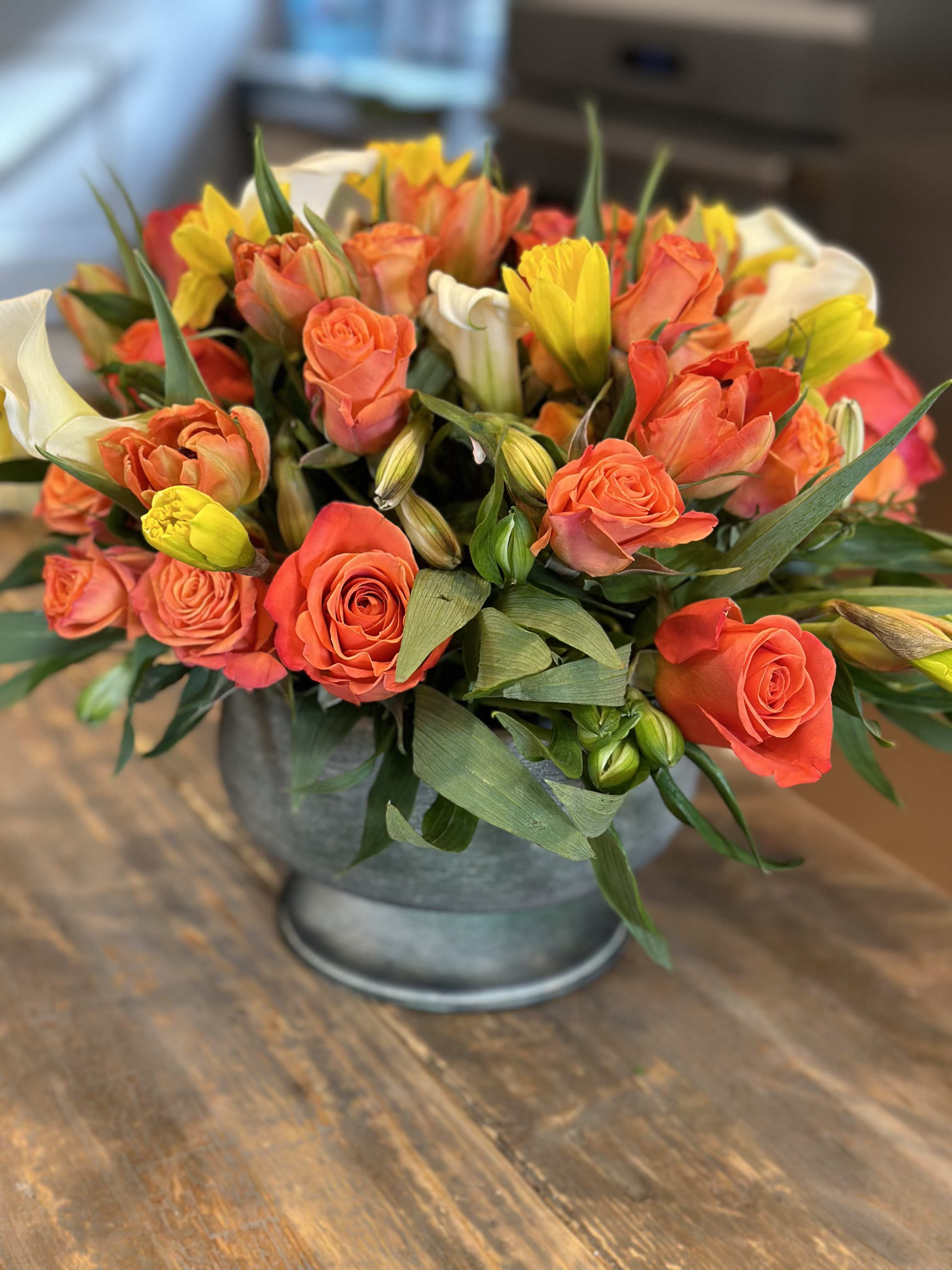 Orange roses and yellow tulips arranged in a metal vase
