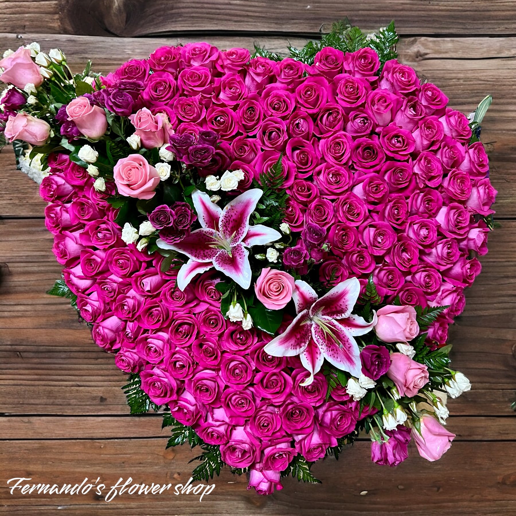 Heart-shaped arrangement of hot pink roses accented with pink roses and pink-white lilies.