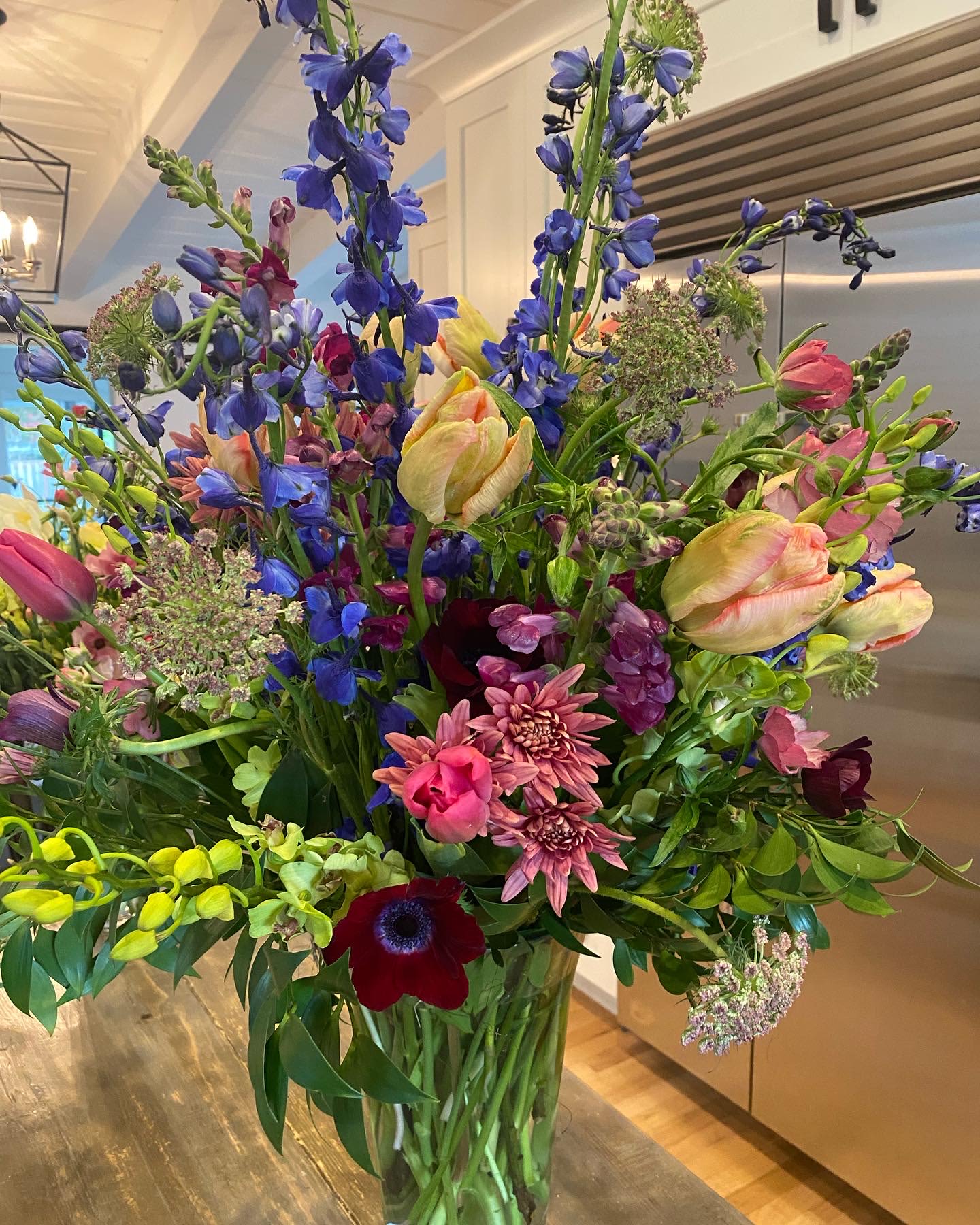 Tall mixed bouquet with blue, pink, yellow, and burgundy flowers in a glass vase