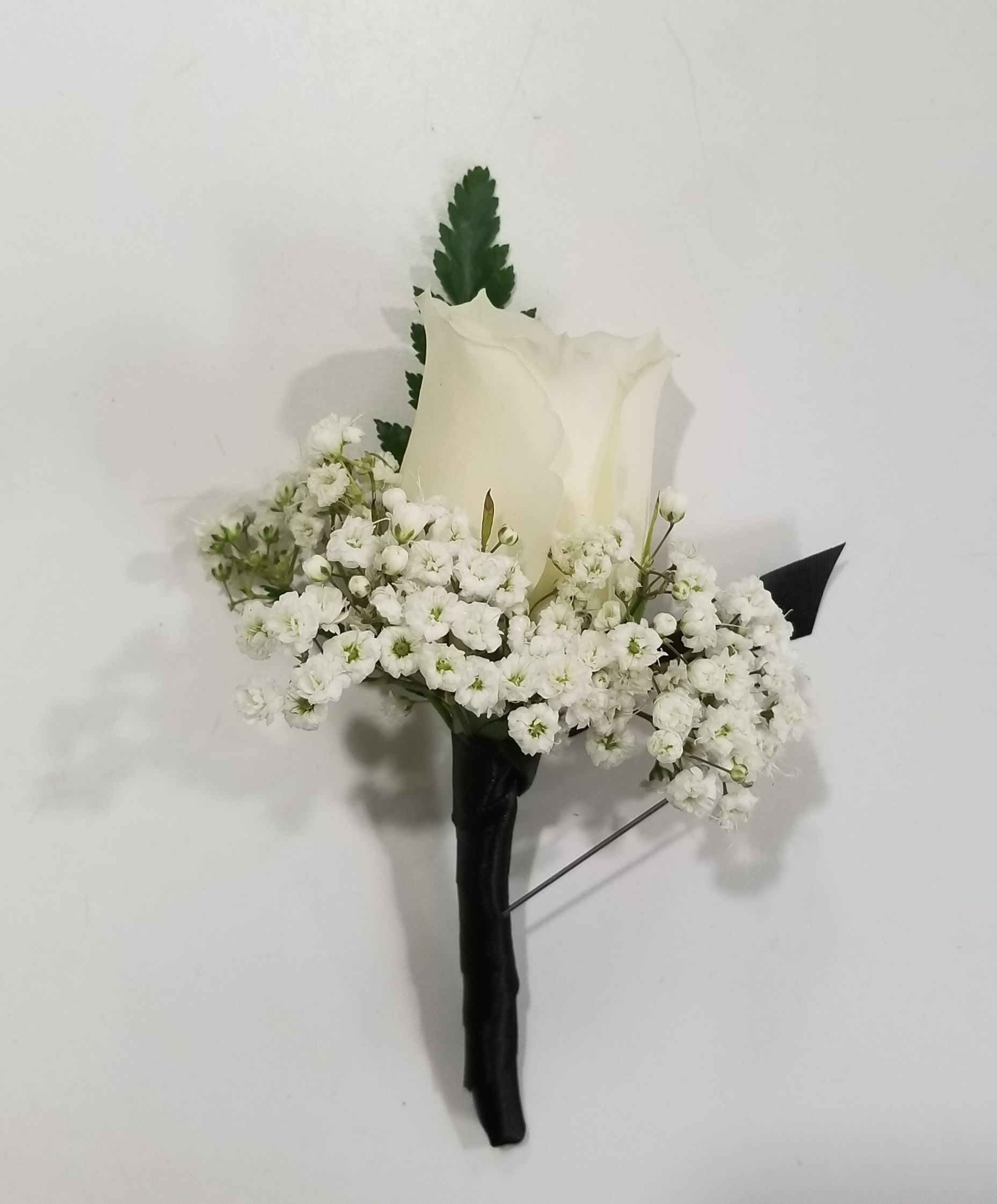 White rose boutonniere with baby's breath and dark greenery