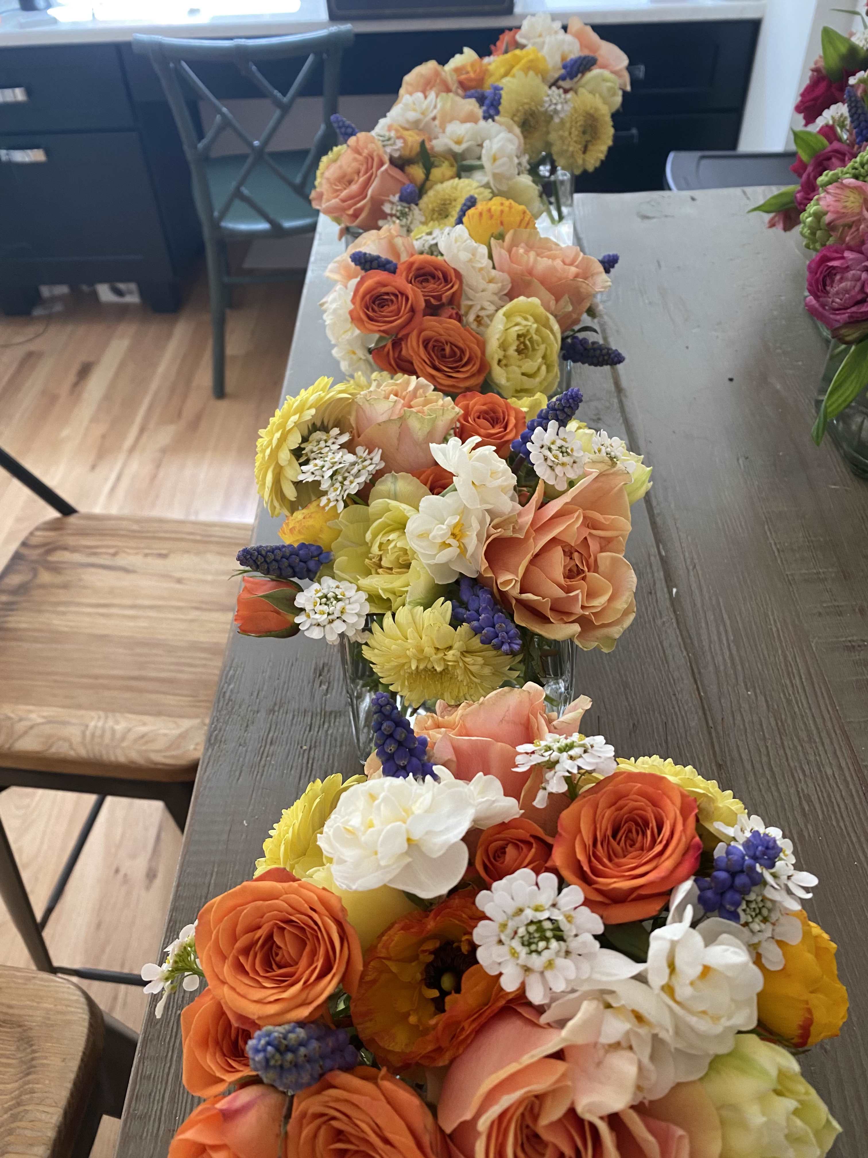 Rows of colorful flower arrangements in clear glass containers on a table