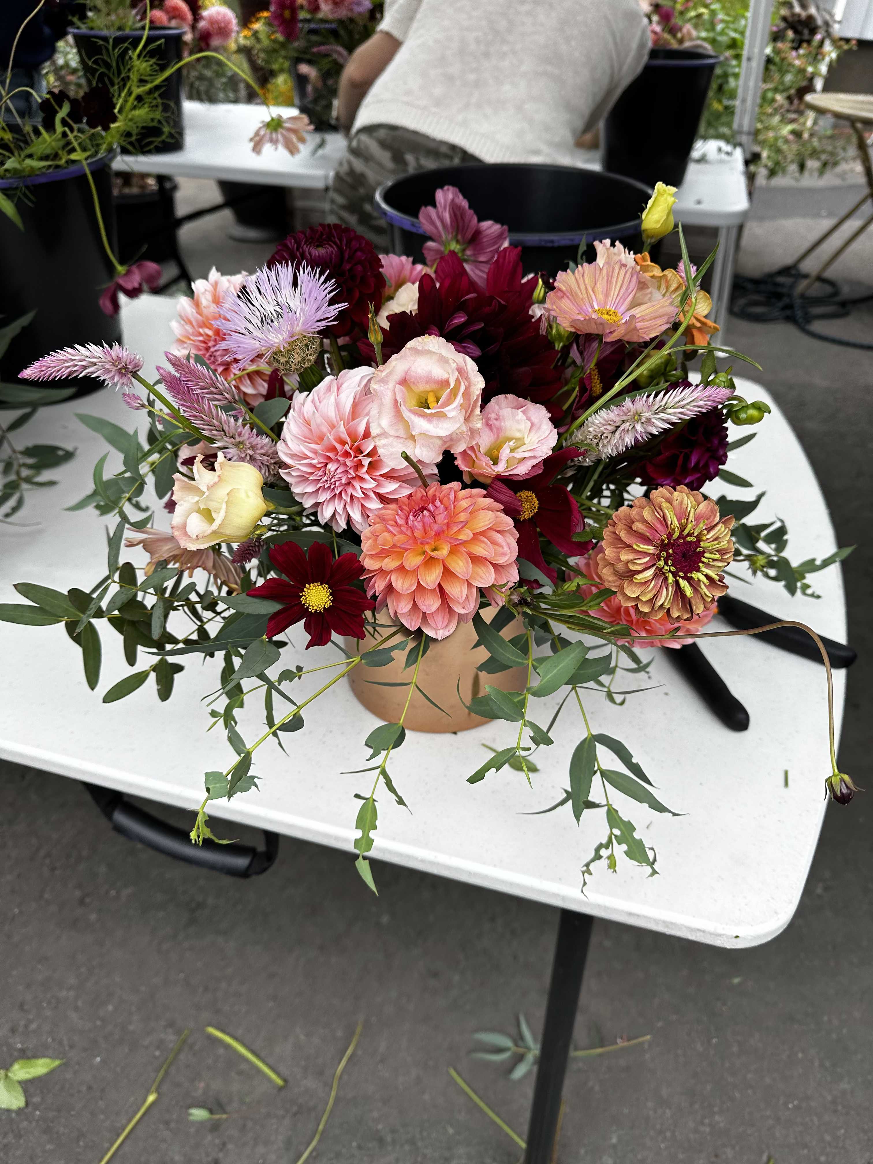Mixed bouquet of pink, peach, and burgundy flowers in a round container