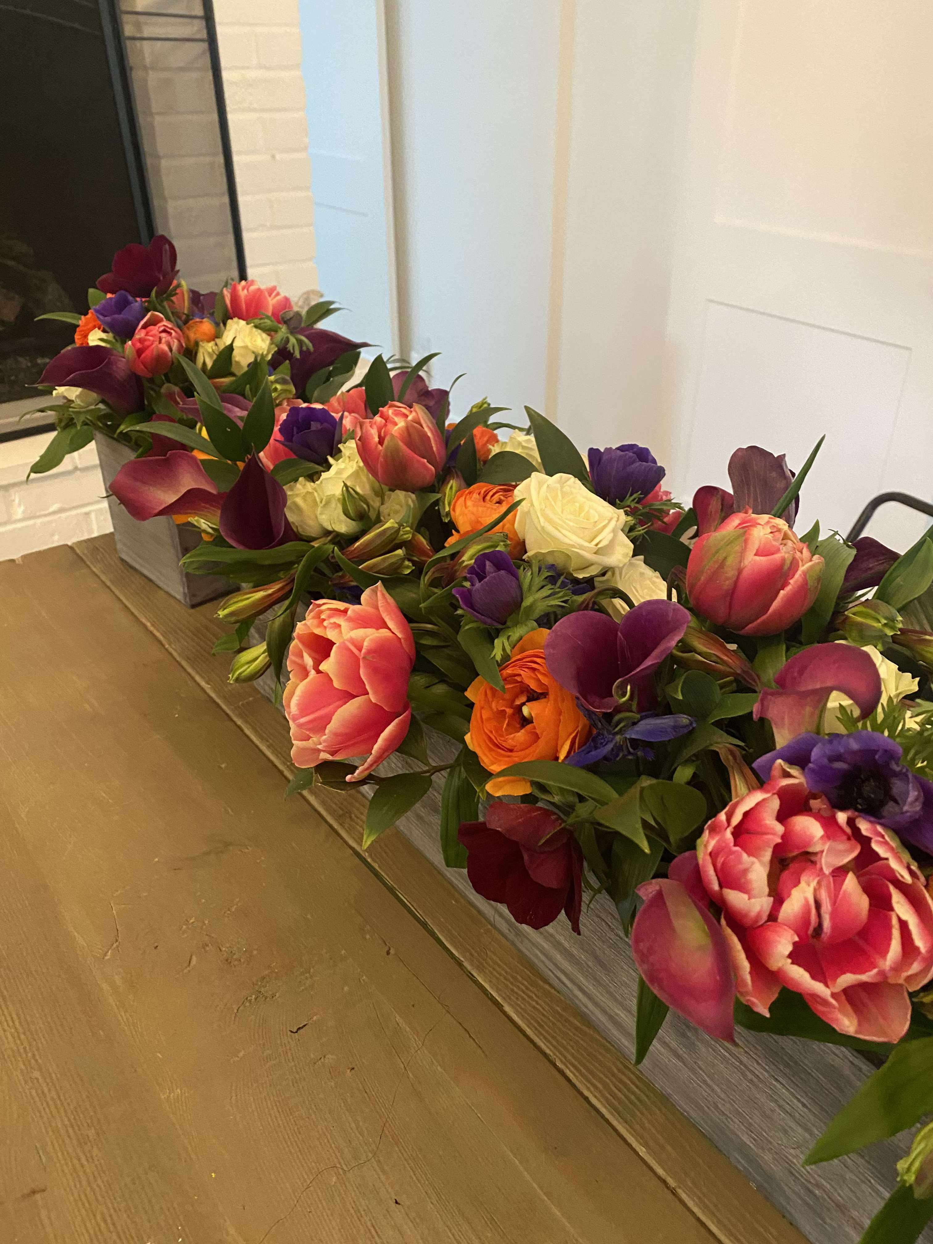 Long low floral arrangement with tulips, roses, calla lilies, and purple blooms