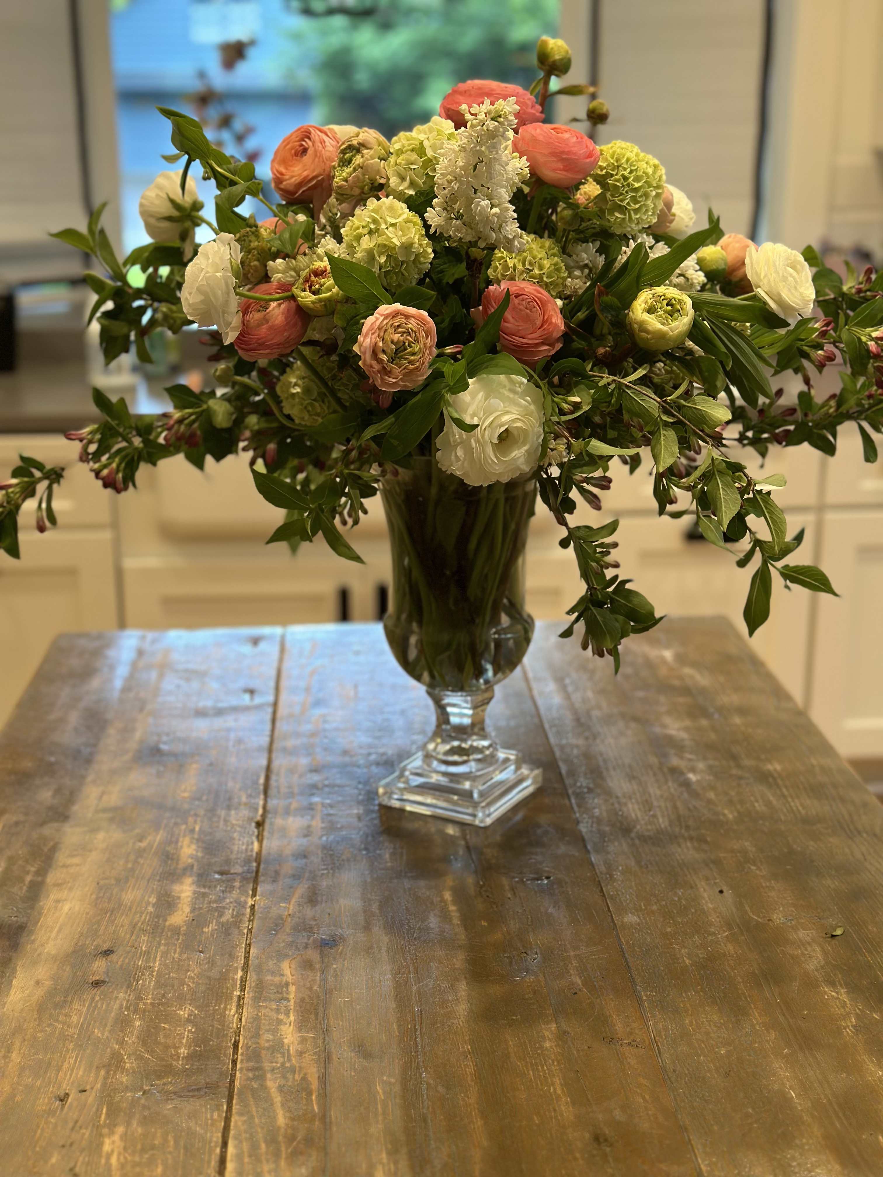 Mixed bouquet of coral, white, and green flowers in a clear glass vase