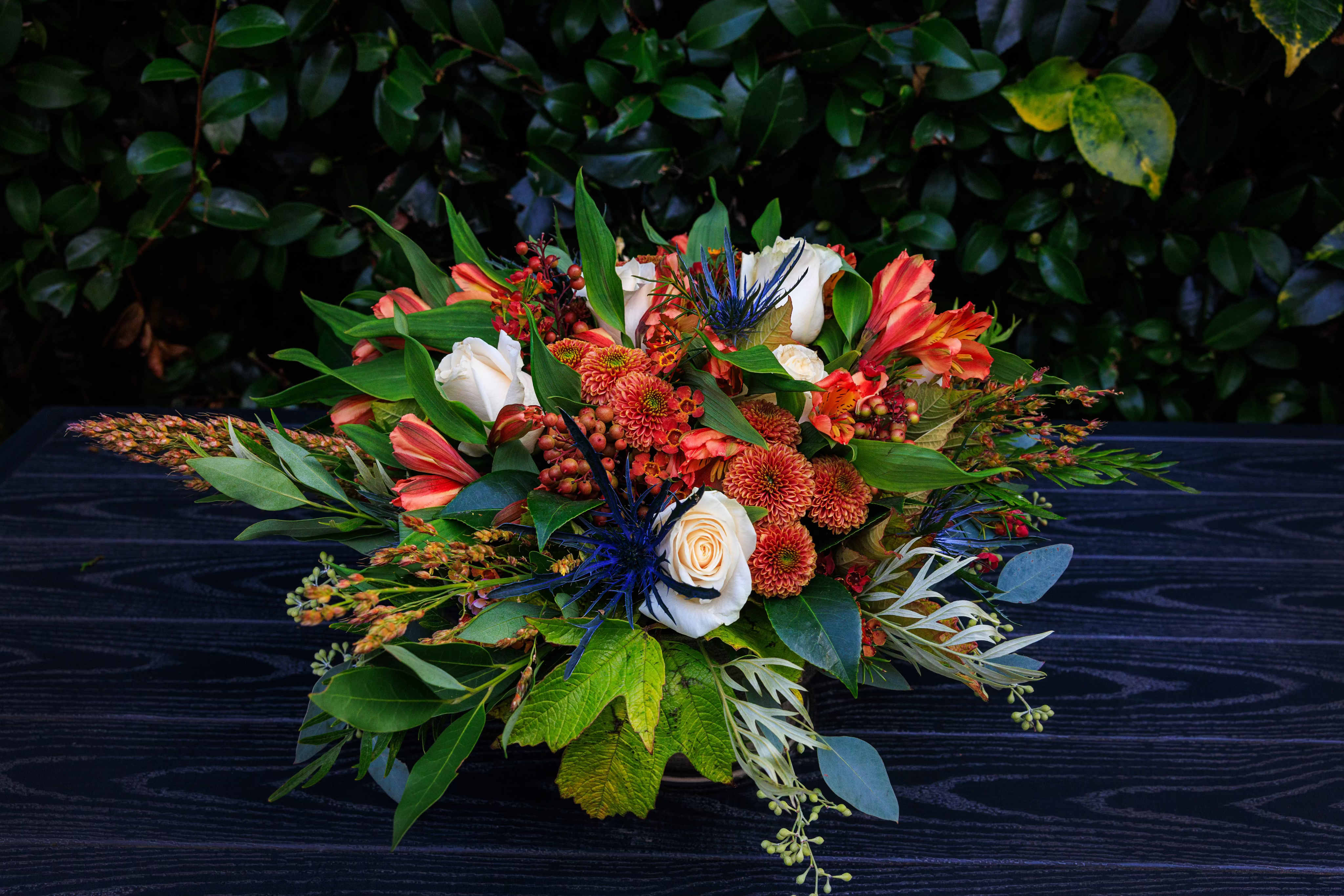 Low floral arrangement with orange, white, and blue blooms on a dark table