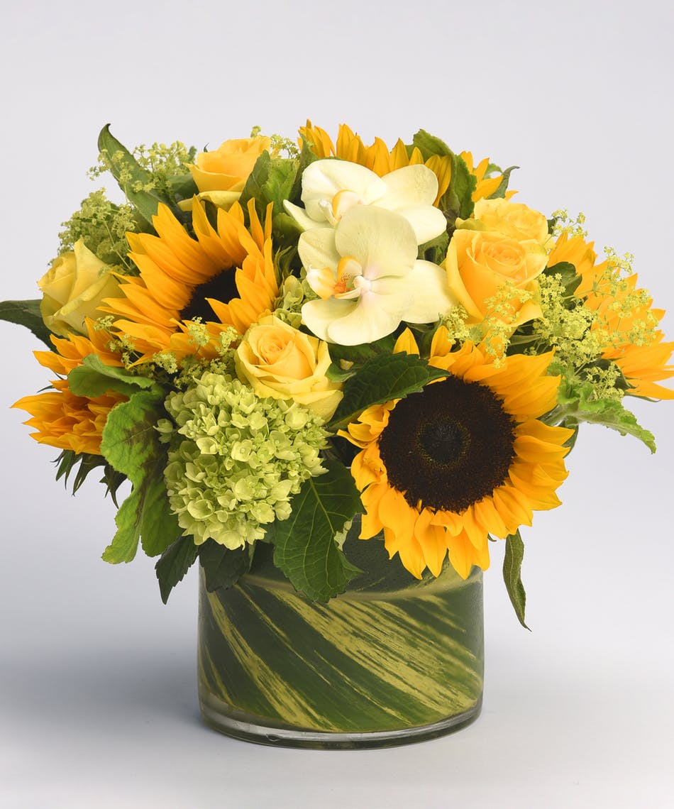 Bouquet of sunflowers, yellow roses, and white orchids in a glass vase