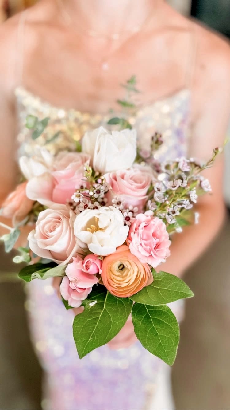 Person holding a small pastel bouquet of pink roses, white blooms, and peach ranunculus.