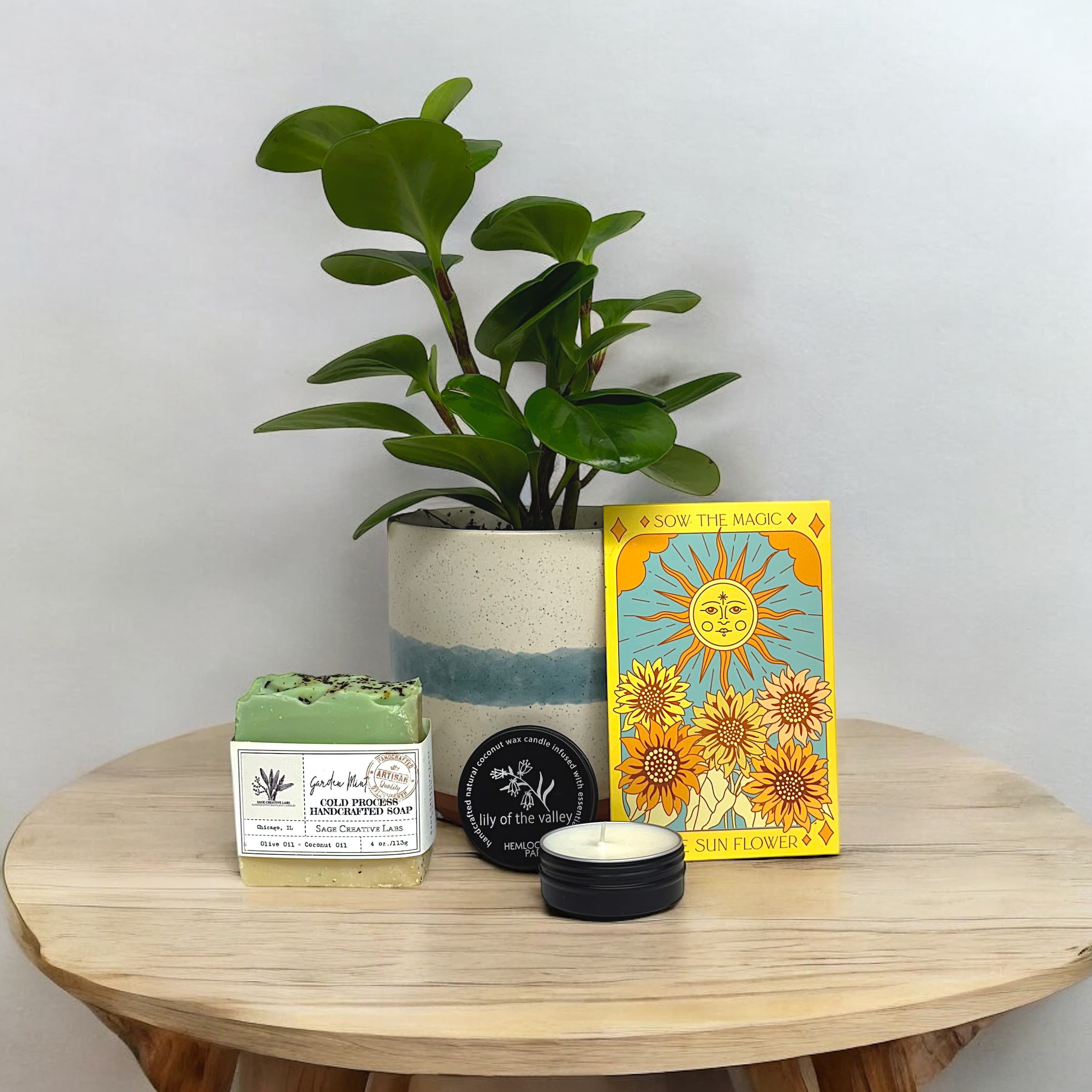 Garden Gift Set - Do you or someone special you know have an excellent green thumb? Then this is the perfect gift set for you! Allow this gift set to enrich your soul with nature as you nurture these seeds and plant.   This gift set includes  plantable sunflower seeds from Sow the Magic in a Tarot Card "The Sun Flower" seed packet.  Hemlock Park mini candle in the scent "Lily of the Valley". A black tin containing coconut wax infused with essential oils.   Sage Creative Labs Soap in the scent "Garden Mint". 4oz bar made with Olive and Coconut Oil infused with natural scents and oils. Soft on Skin.c  Also included is a variegated Peperomia plant in a 4in ceramic pot. 