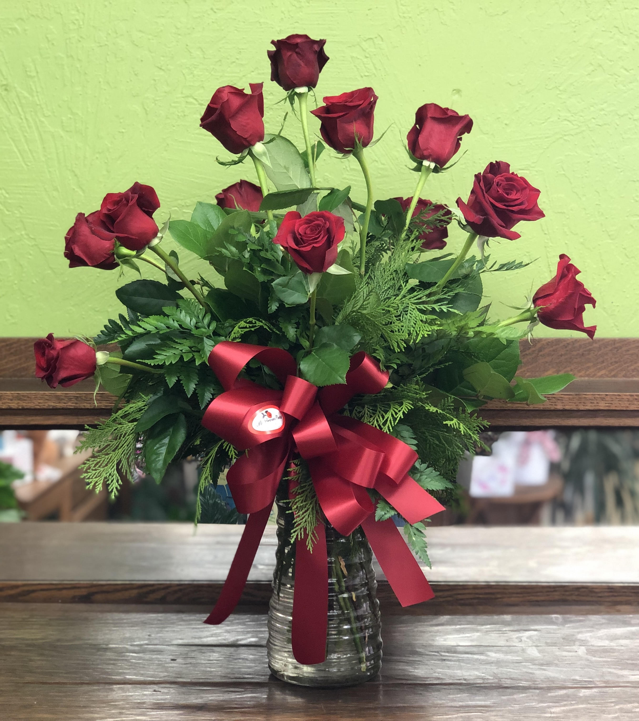 Arrangement of long-stemmed red roses in a clear glass vase with a large red bow.