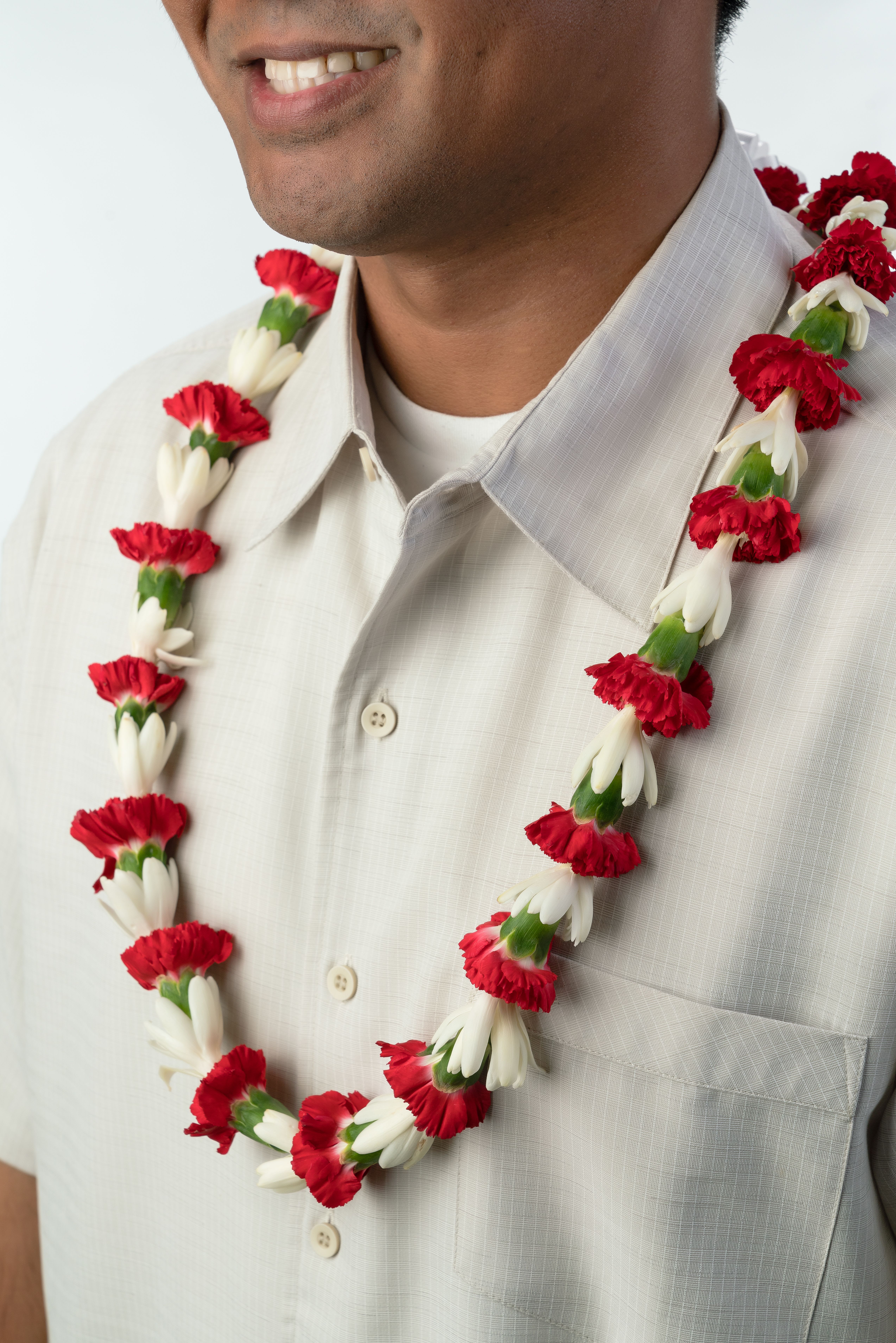 Red and white flower lei worn around a person’s neck over a light collared shirt