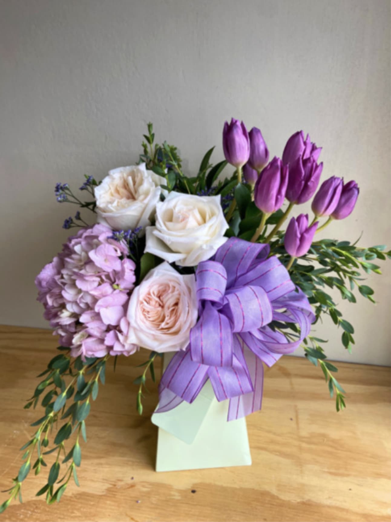 Bouquet of white roses, purple tulips, and lavender flowers in a white box