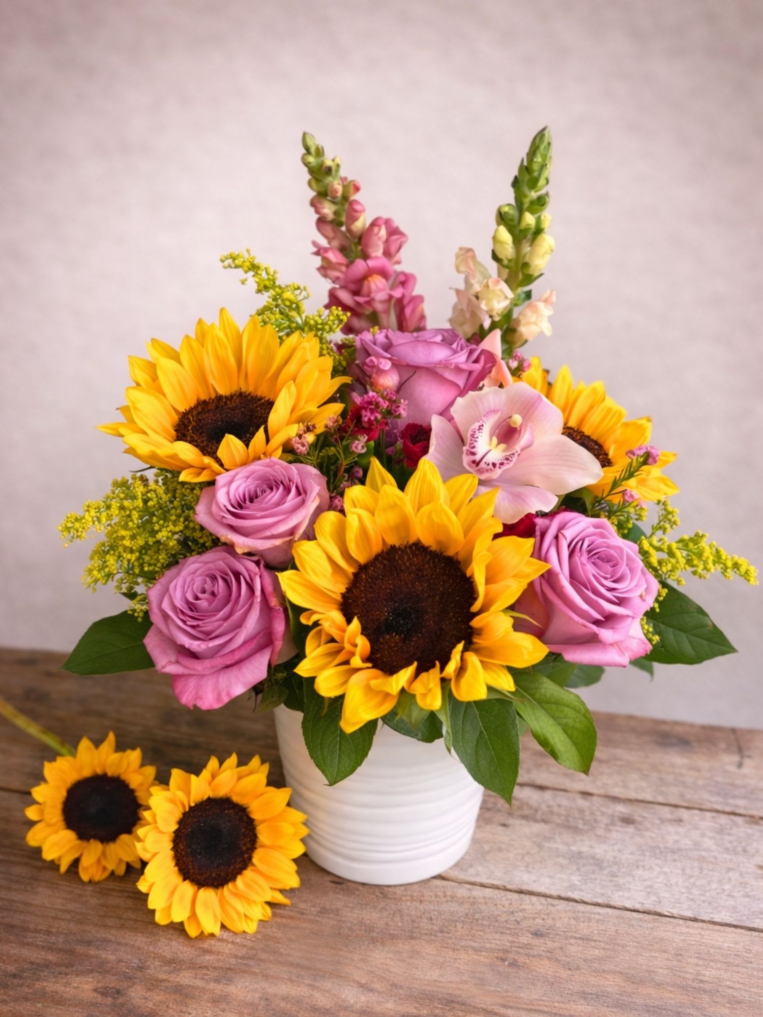 Bouquet of sunflowers and lavender roses in a white vase
