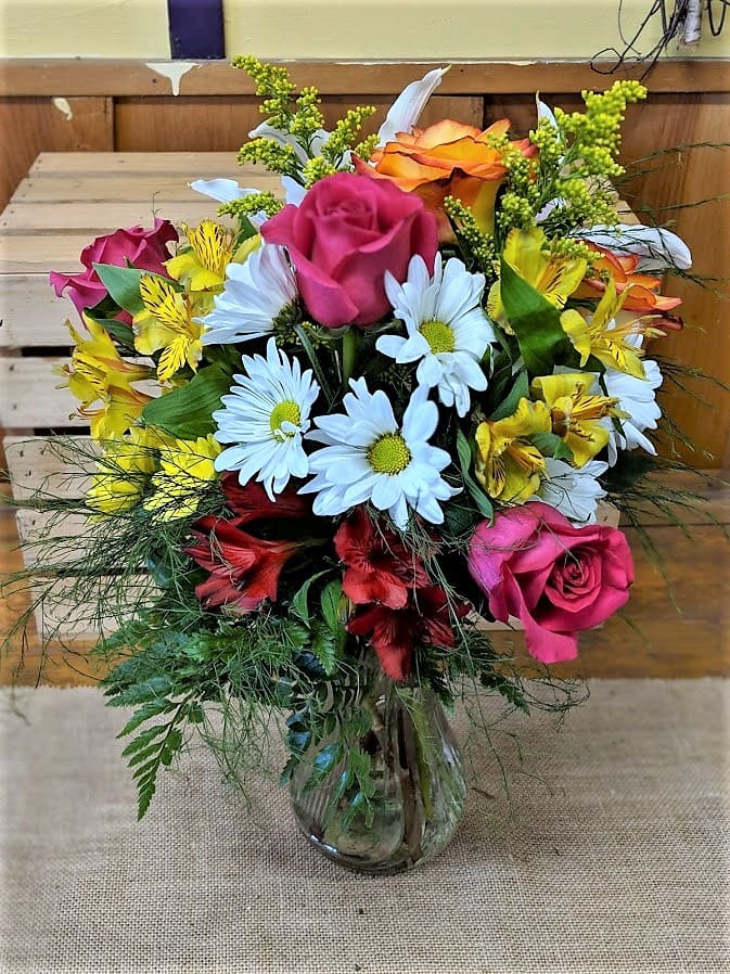 Mixed bouquet of roses, daisies, and yellow alstroemeria in a glass vase