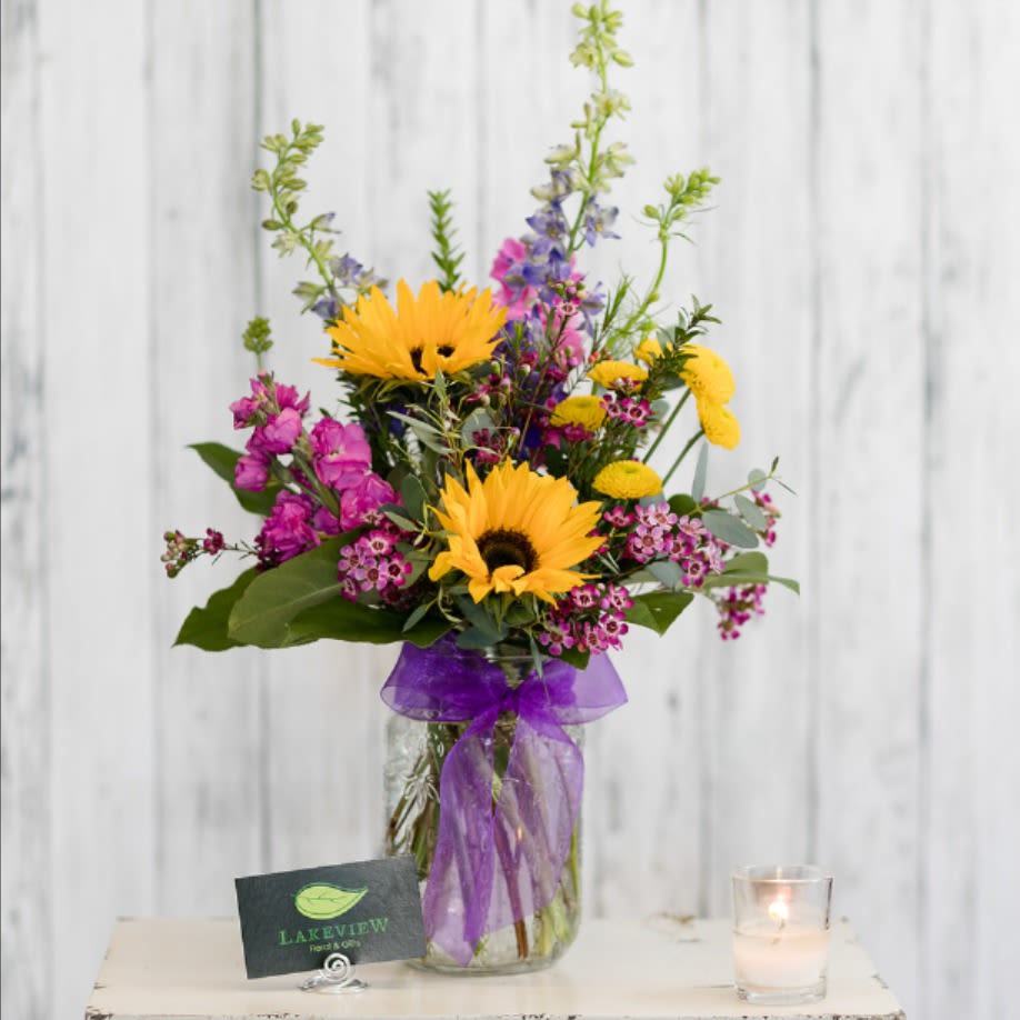 Countryside - Reminiscent of blooms gathered from a bright garden path, an heirloom mason jar overflows with larkspur, sunflowers and fragrant stock.    Approximate Dimensions: 19" H x 12" W