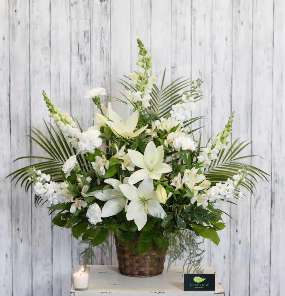 White floral arrangement in a woven basket with a candle beside it