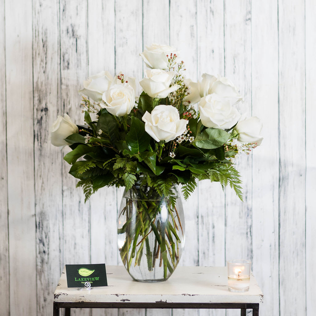 White roses arranged in a clear glass vase with greenery