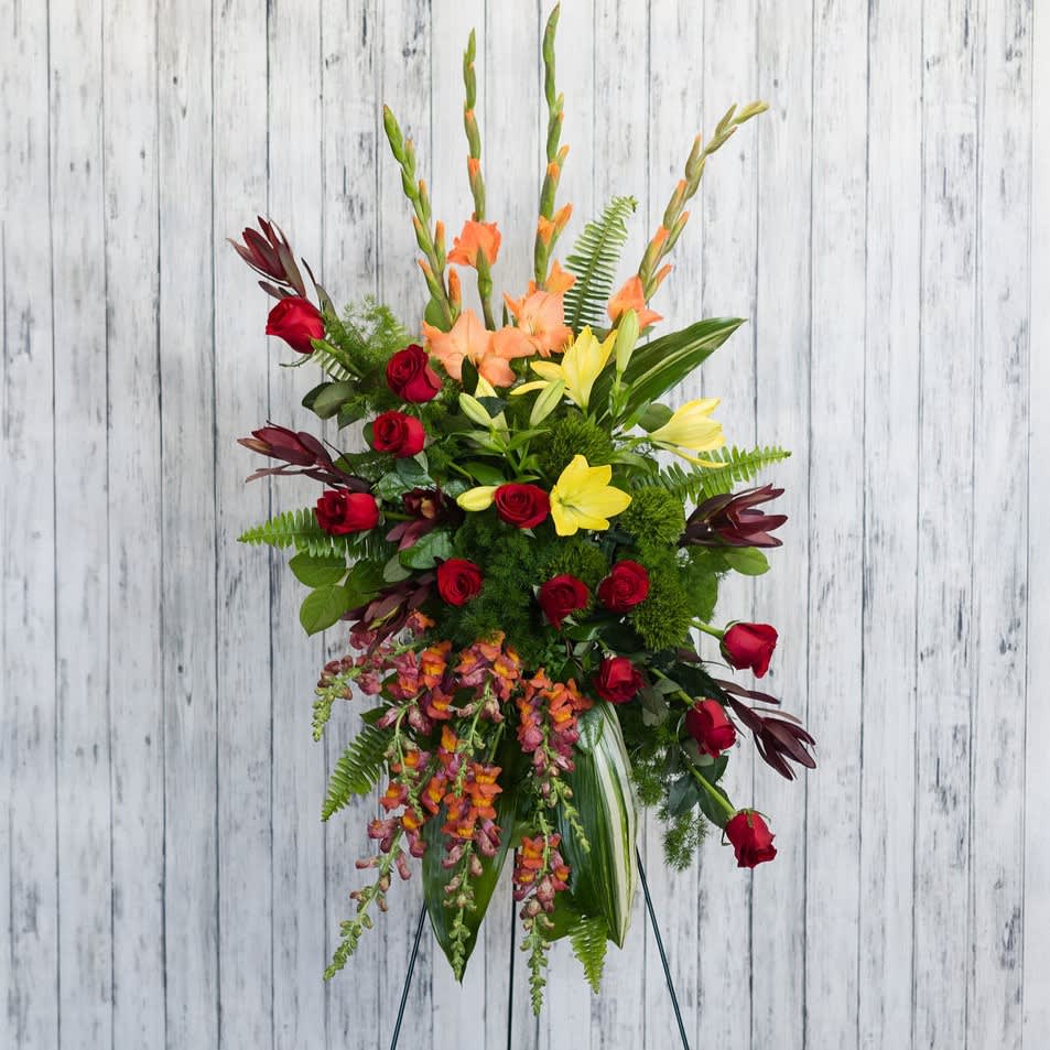 Tall floral arrangement with red roses, yellow lilies, and orange blooms