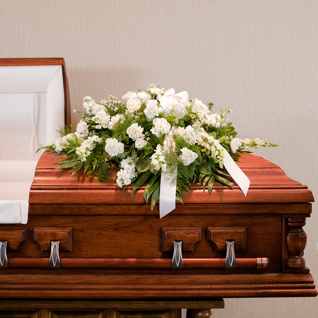 White floral spray on a wooden casket with ribbon accents