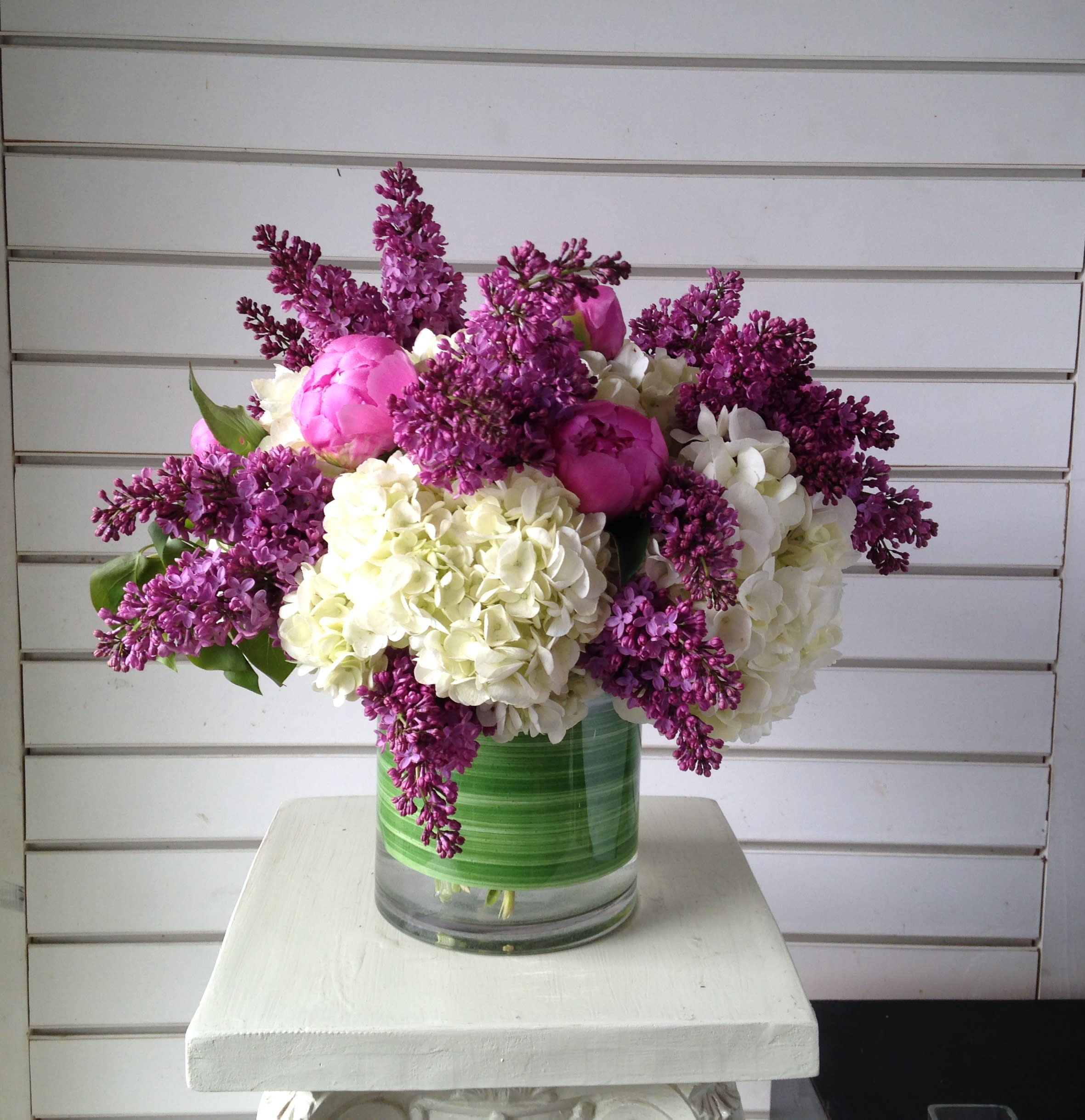 Pink peonies and white hydrangeas in a glass vase with purple lilacs