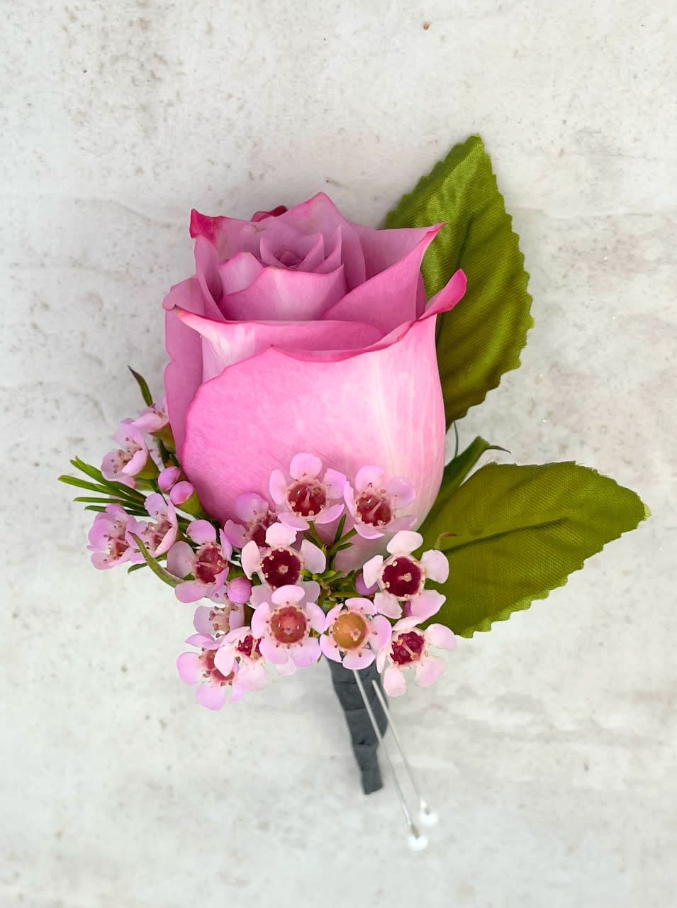 Pink rose boutonniere with small pink blossoms and green leaves