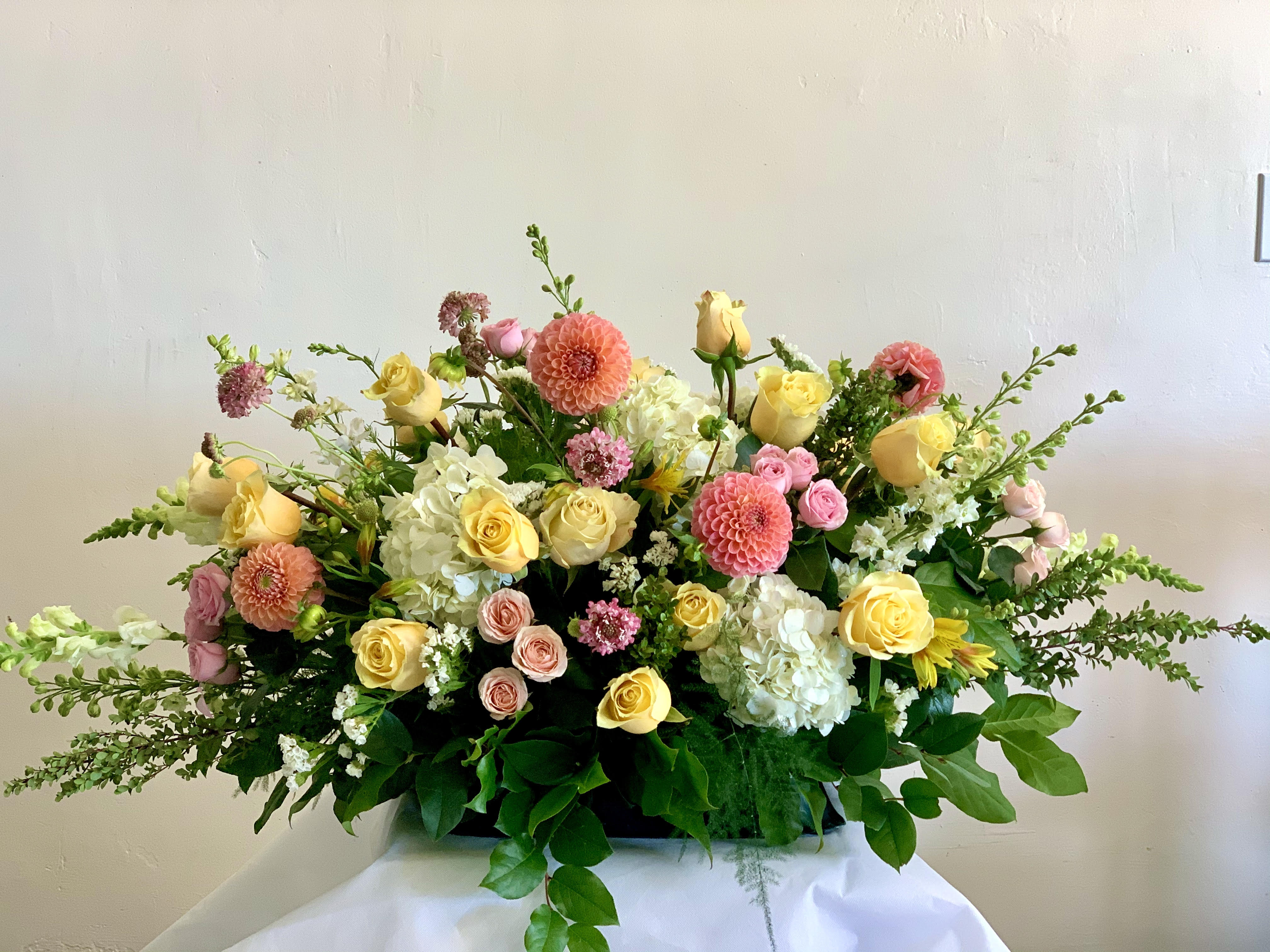Large pastel floral arrangement with roses, dahlias, and hydrangeas in a low container