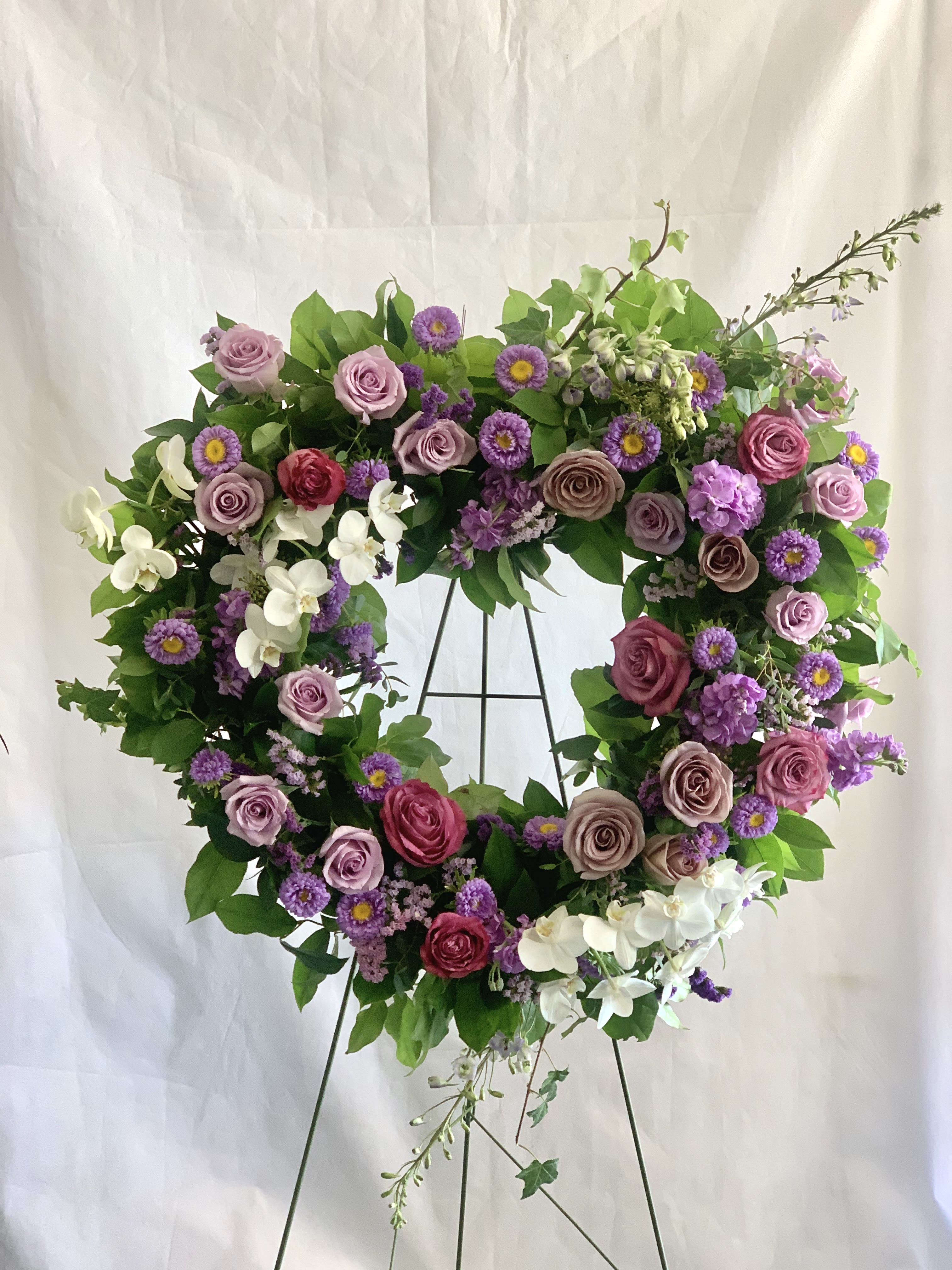 Heart-shaped floral wreath with pink and purple flowers on a metal stand