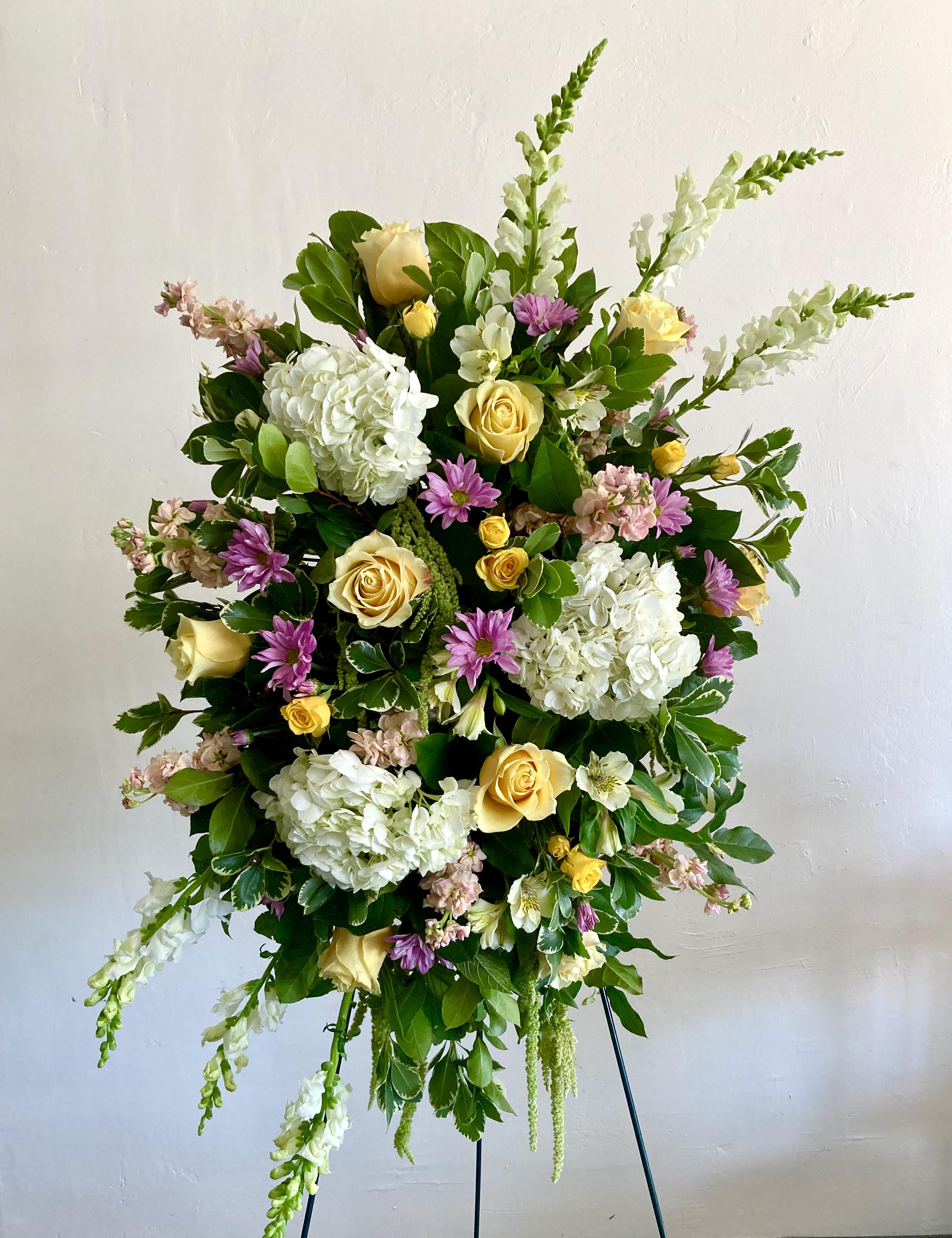 Standing floral spray with yellow roses, white hydrangeas, and purple blooms