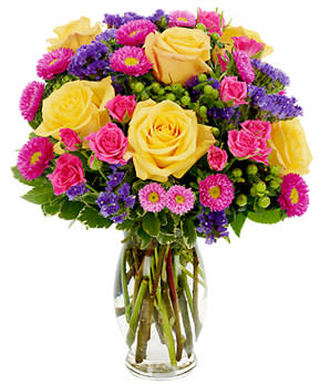 Bouquet of yellow roses, pink flowers, and purple blooms in a glass vase