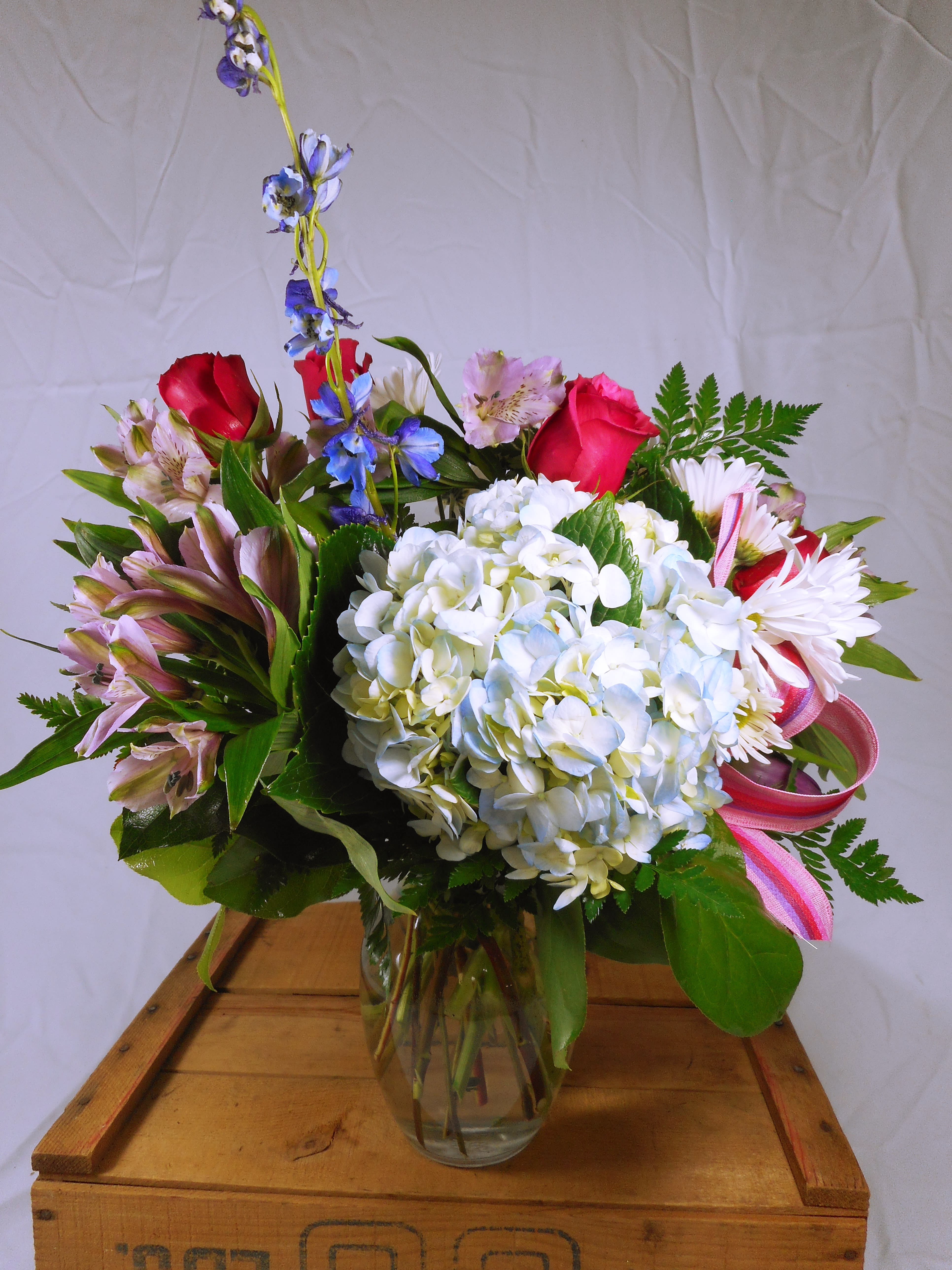 Mixed bouquet of roses, hydrangea, and daisies in a glass vase