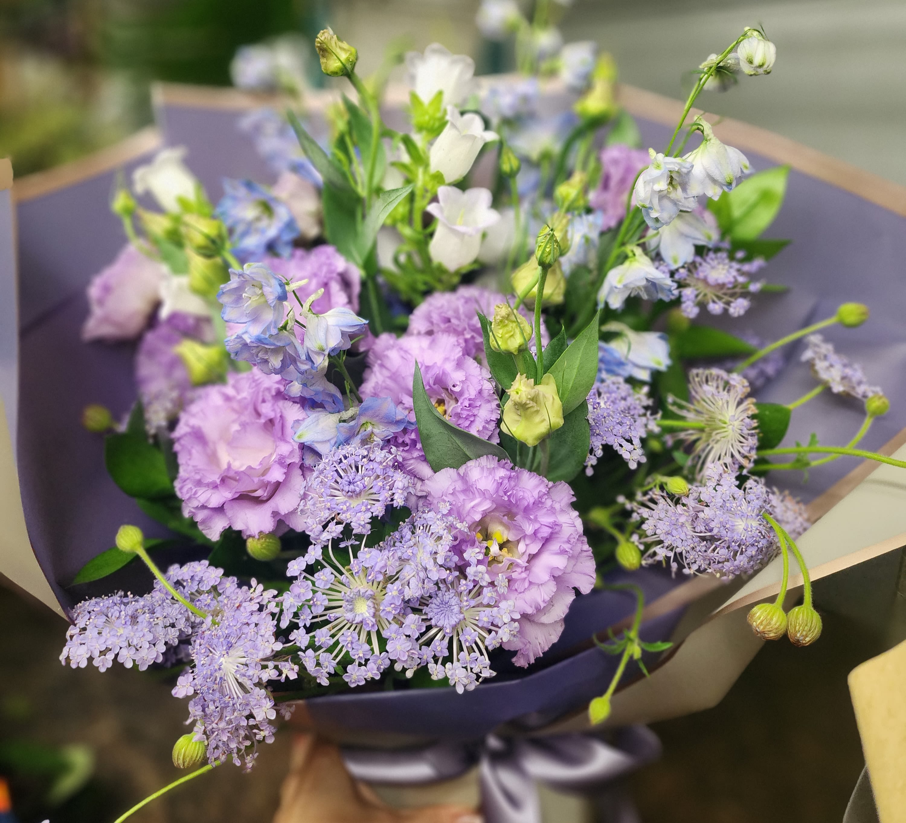 Lavender and white bouquet with airy blue flowers wrapped in dark paper
