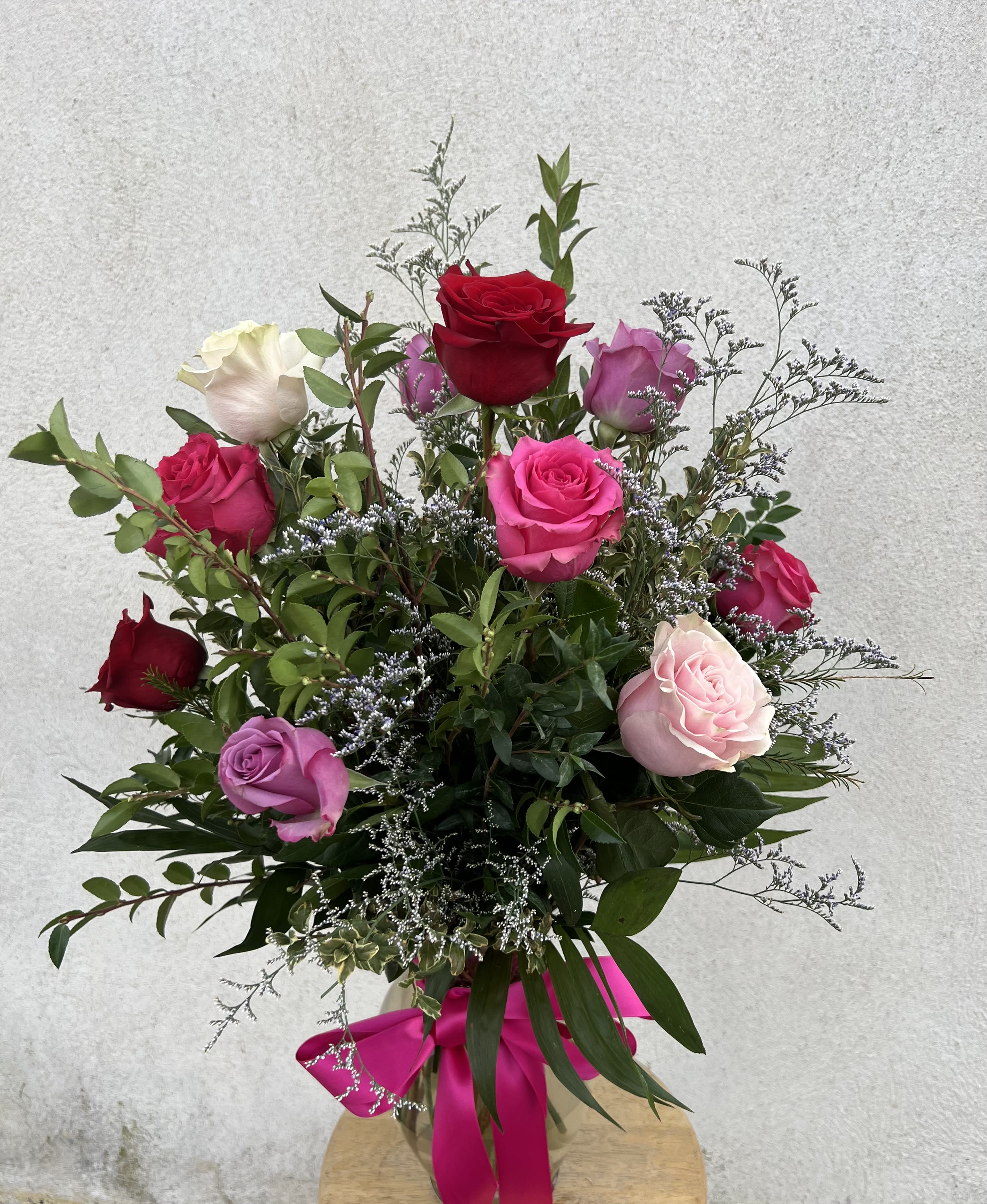 Tall mixed arrangement of red, pink, and lavender roses in a glass vase with a pink bow