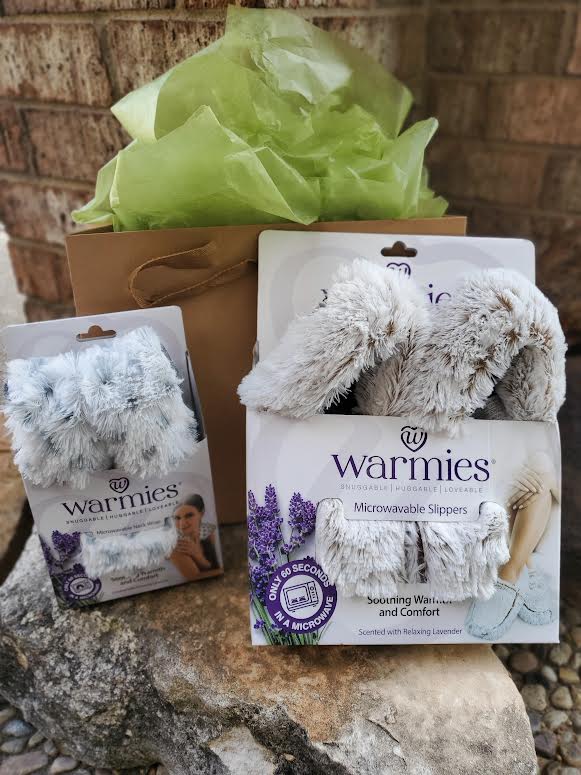 Gift set with two pairs of fuzzy slippers in packaging and a brown bag with green tissue paper