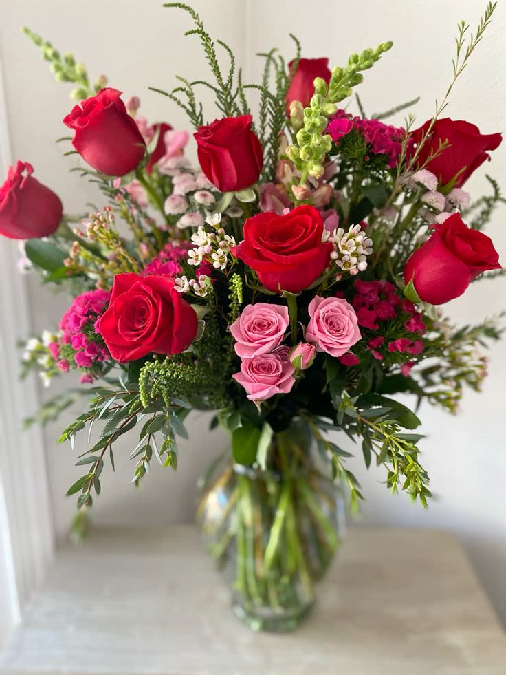 ROSEY CHEEKS &amp; WARM HEARTS - A tall, layered bouquet of red and pink roses that reads like a classic love note-perfect as an anniversary bouquet, Valentine's Day gift, or a radiant birthday surprise. The mix of strong red tones with softer pink accents creates a romantic yet approachable look that will make the person you're thinking of feel cherished and celebrated.  This flower arrangement pairs densely clustered roses with small white filler blooms and airy branching greenery for contrast and texture. Roses are arranged at varying heights to create an abundant, full silhouette and arrive in a clear glass vase that showcases the stems and keeps the display simple and elegant. Ideal for sending warm wishes or romantic sentiments, it's the kind of bouquet that looks impressive on a dining table or bedside-order sized to arrive ready-to-display; trim stems and refresh water every couple of days to extend vase life.