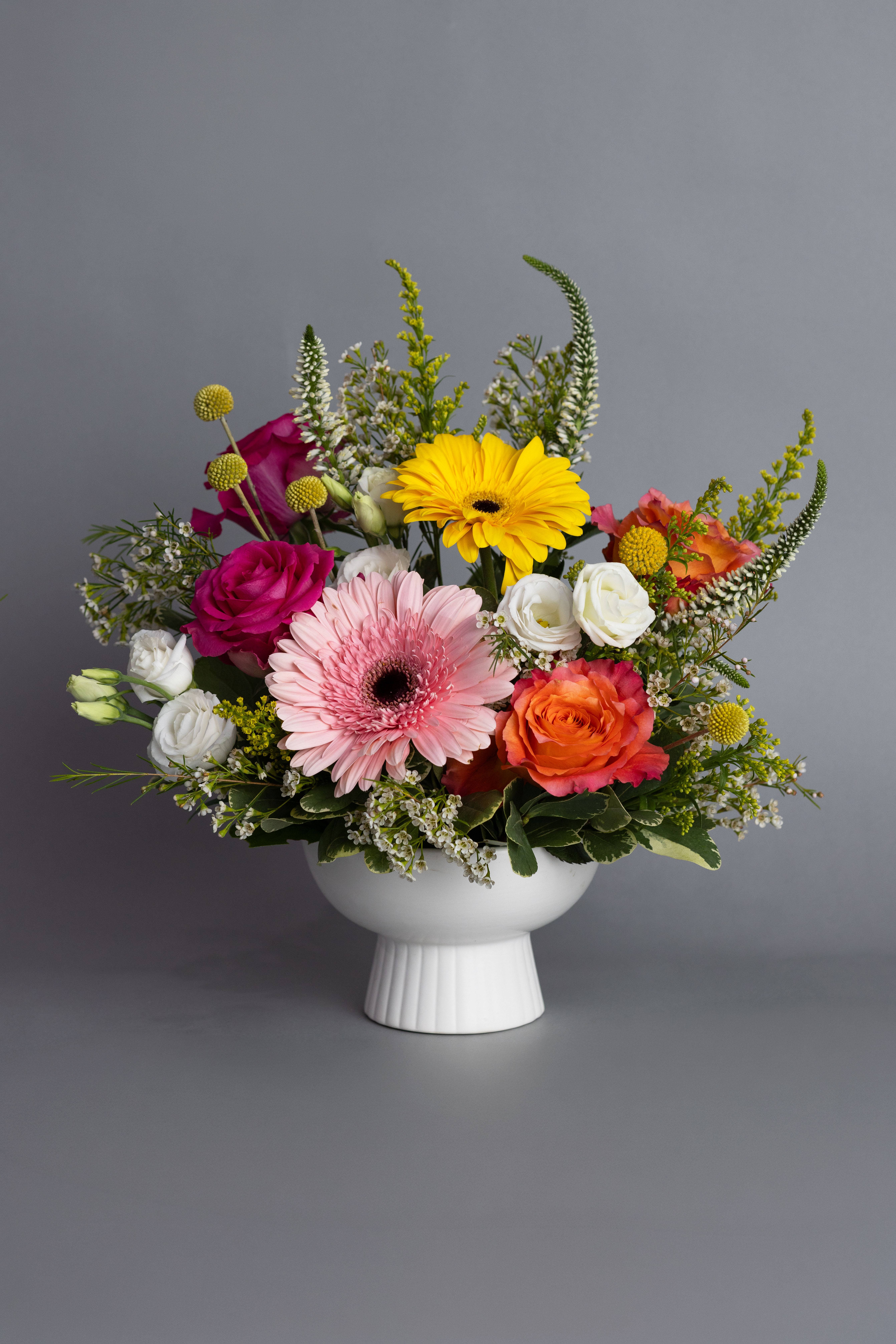 Colorful mix of gerbera daisies, roses, and lisianthus in a white pedestal bowl