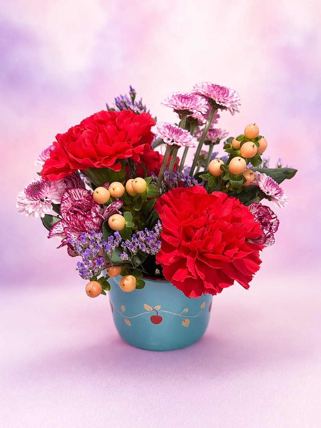 Cherry Pop Charm - A playful and eye-catching arrangement bursting with rich hot pink carnations, delicate lavender accents, and whimsical pink blooms. Tucked into a charming blue keepsake container, this design is finished with soft peach berries and textured greenery for a fresh, garden-inspired feel. Bright, cheerful, and full of personality, it’s the perfect pick-me-up gift or a sweet way to celebrate any day