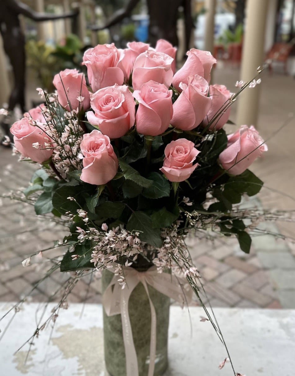 Tall arrangement of pink roses with delicate filler flowers in a glass vase tied with a ribbon