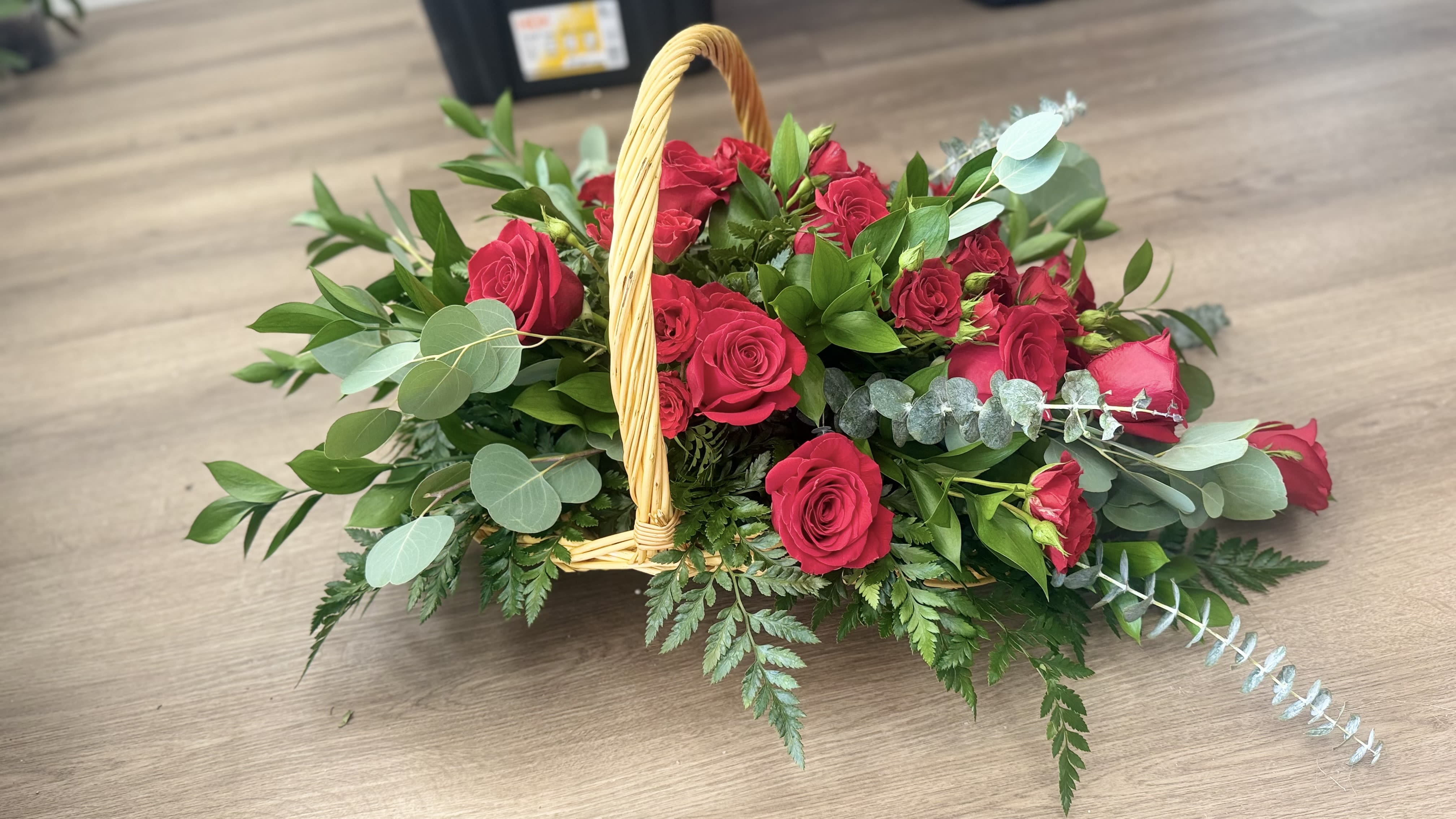 Low wicker basket arrangement of red roses with abundant foliage