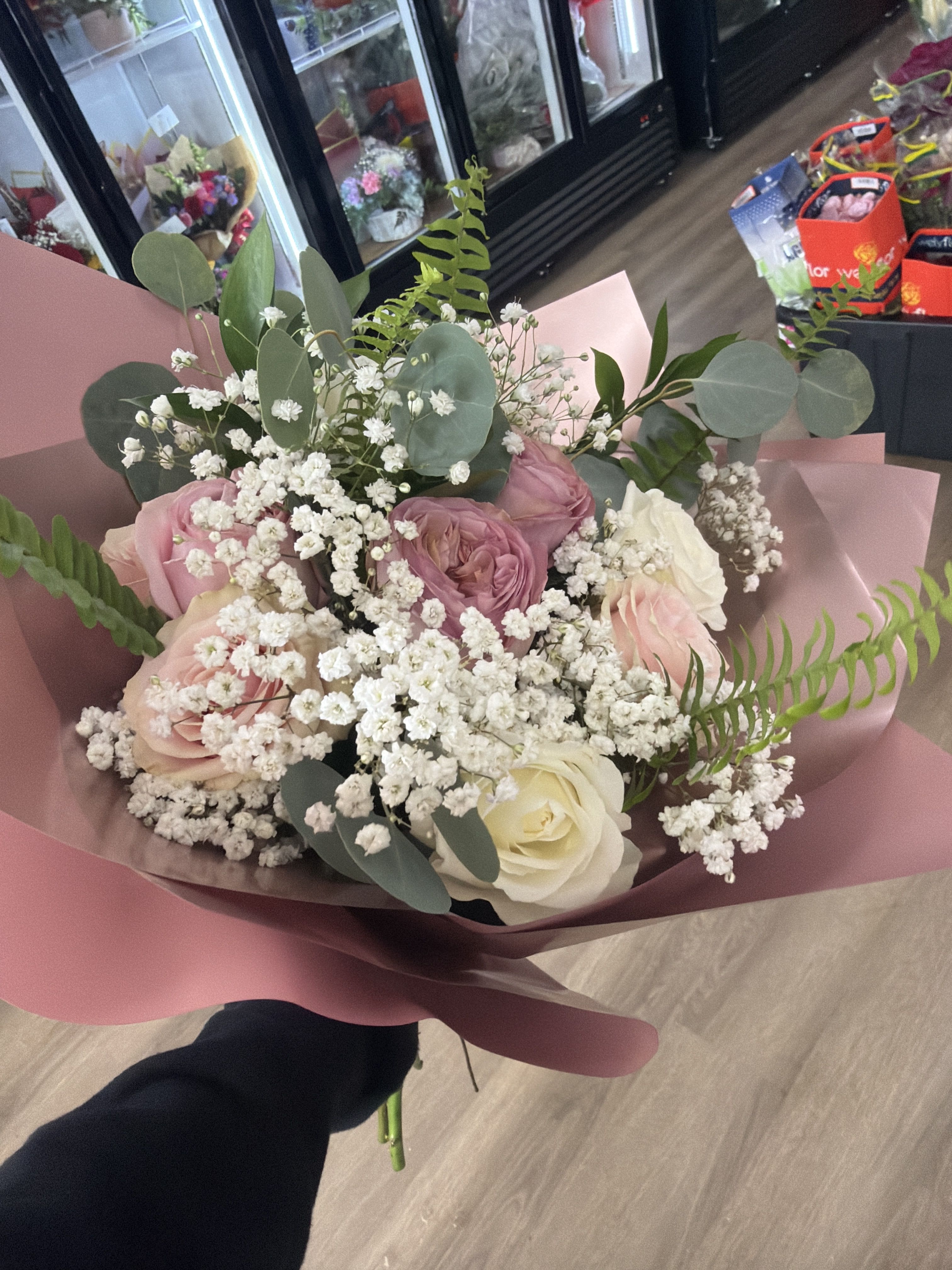 Handheld bouquet of pink and white roses with white filler flowers wrapped in pink paper.