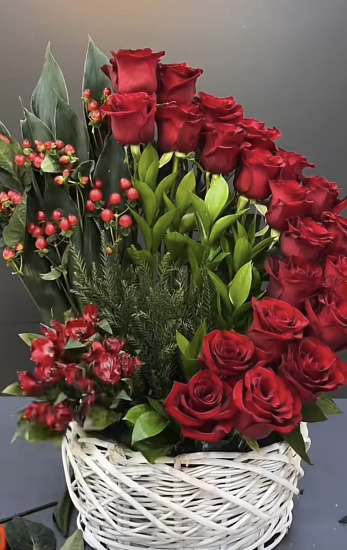 Tall arrangement of red roses with greens in a white woven basket