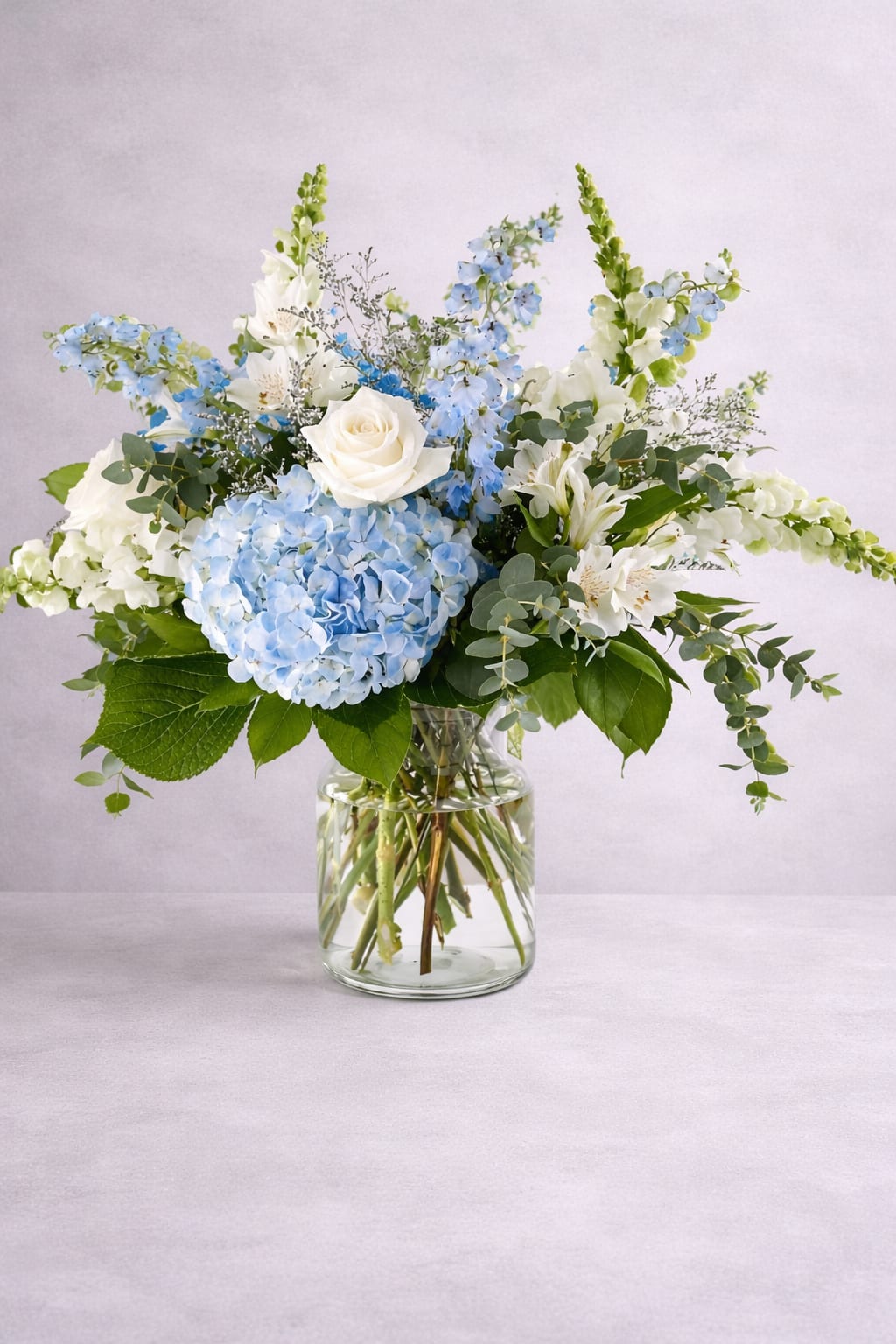 Blue hydrangea and white rose arrangement in a glass vase