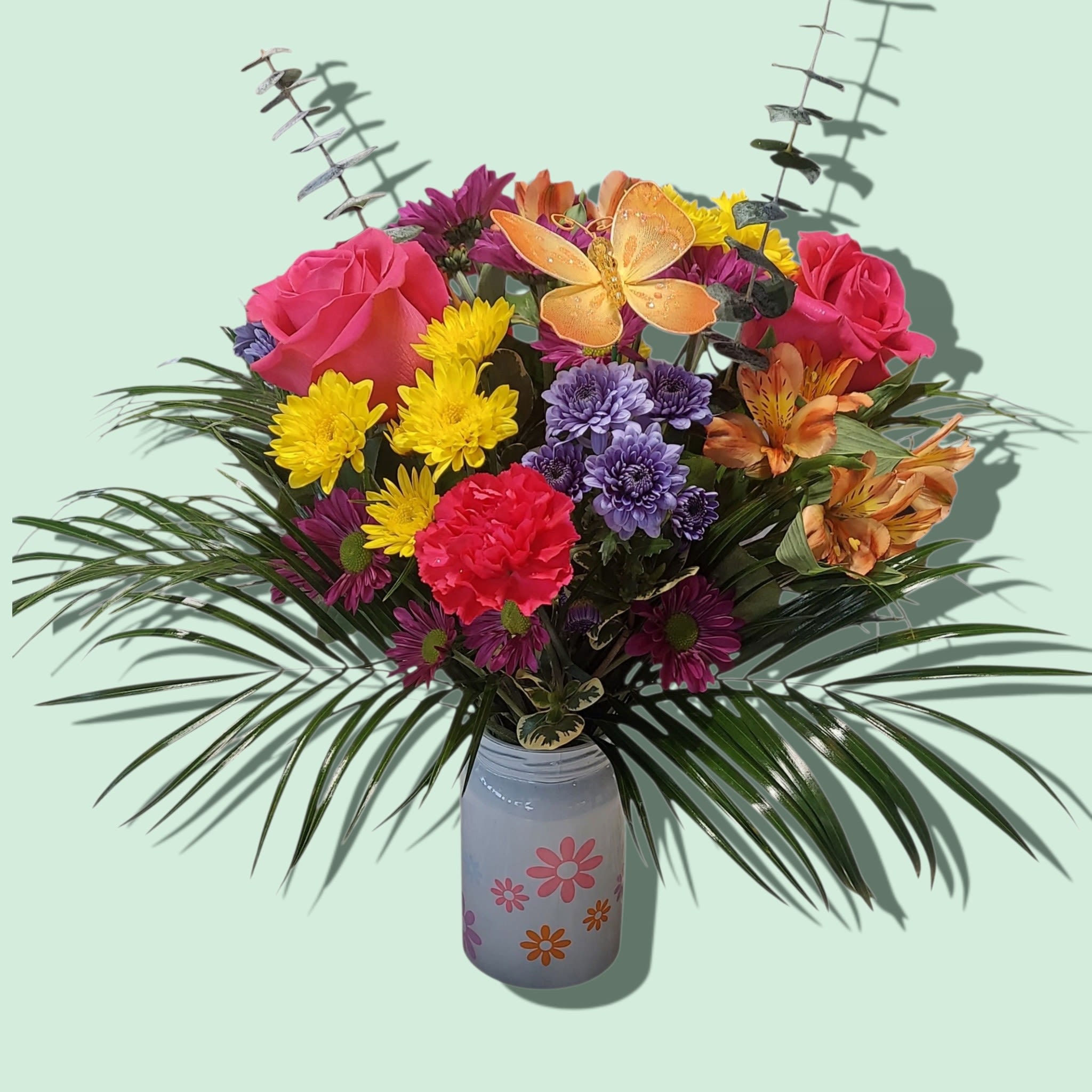 Daisy Bell - Bright mixed roses, mums, carnation &amp; alstroemeria in a painted glass jar with a playful butterfly pick. COLOR OF FLOWERS AND BUTTERFLY WILL VARY. Approximate size: 15W x 16H