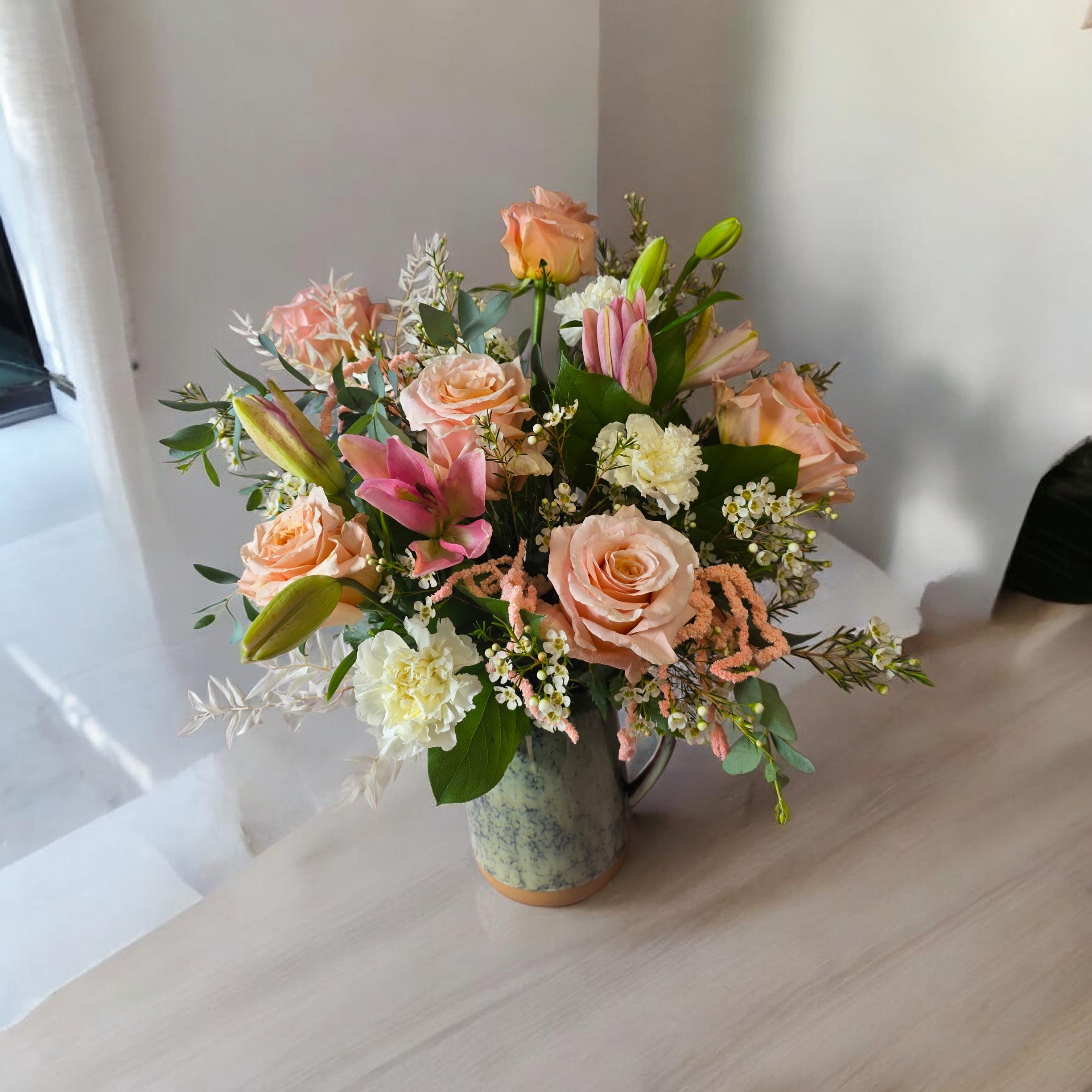 Peach roses and pink lilies arranged in a ceramic pitcher vase
