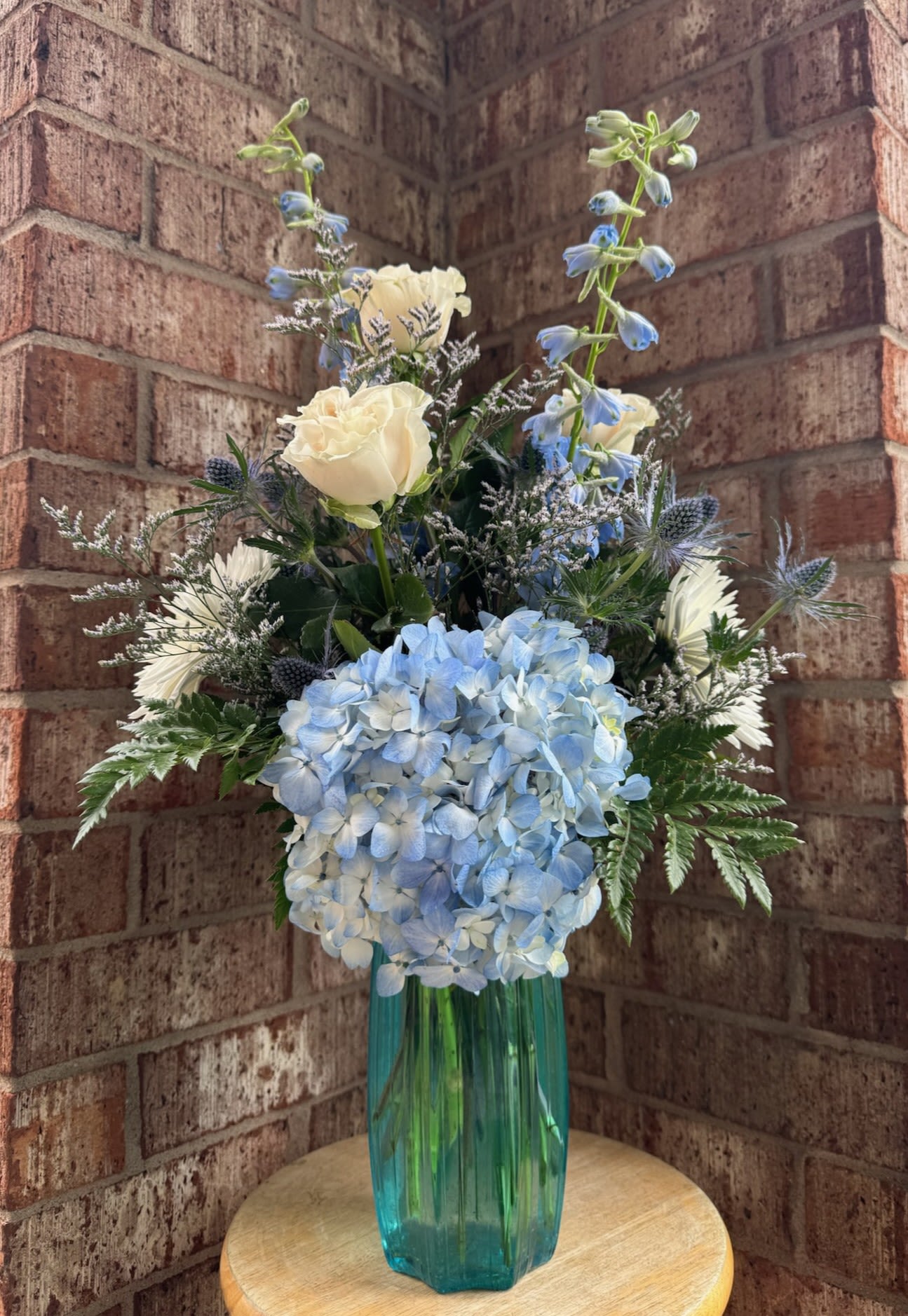 Blue hydrangea and white rose arrangement in a teal glass vase
