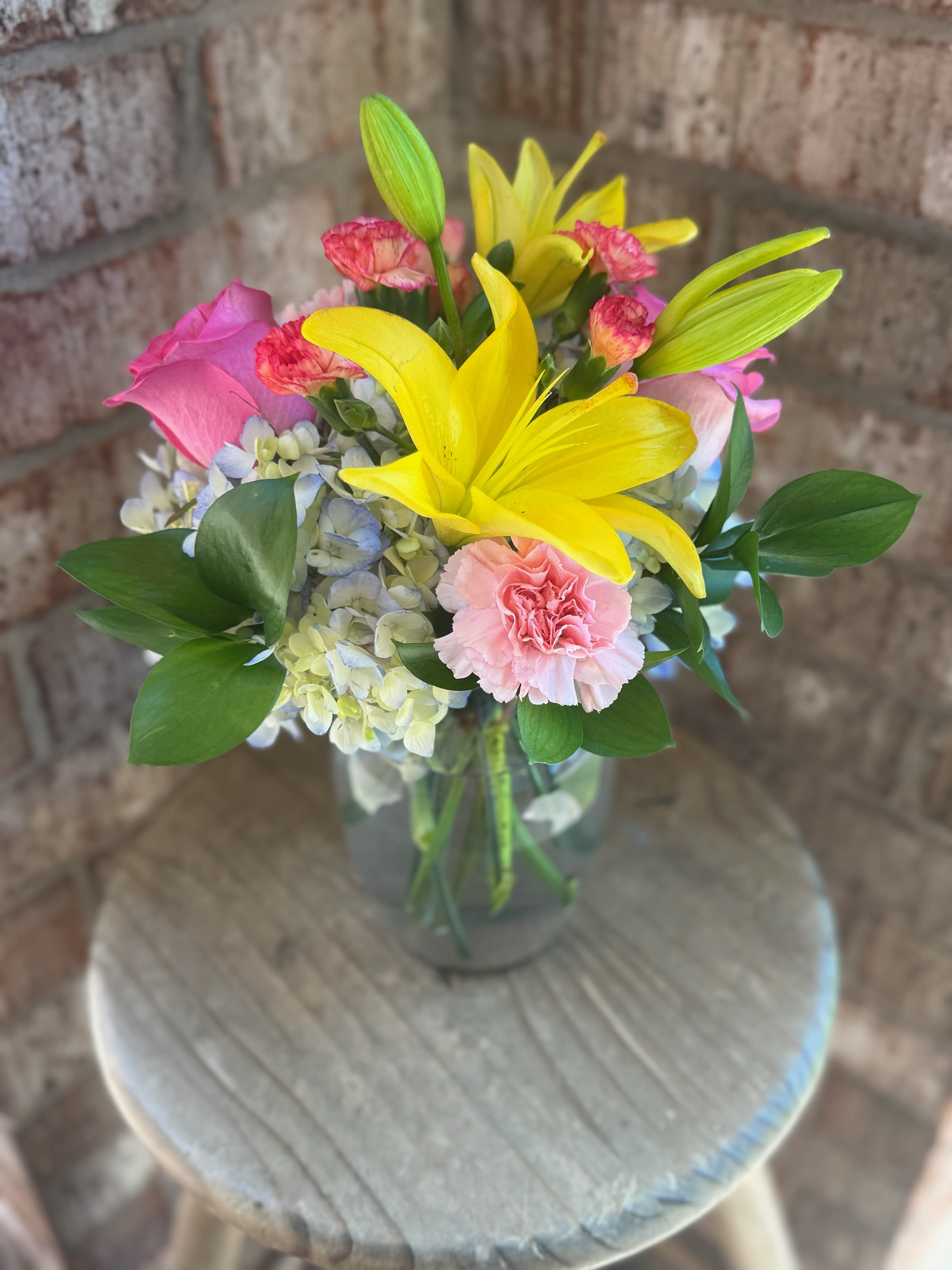 Bouquet of yellow lilies, pink roses, and carnations in a glass vase