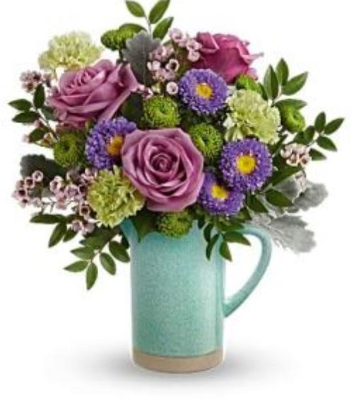 Purple roses and mixed blooms arranged in a turquoise pitcher vase